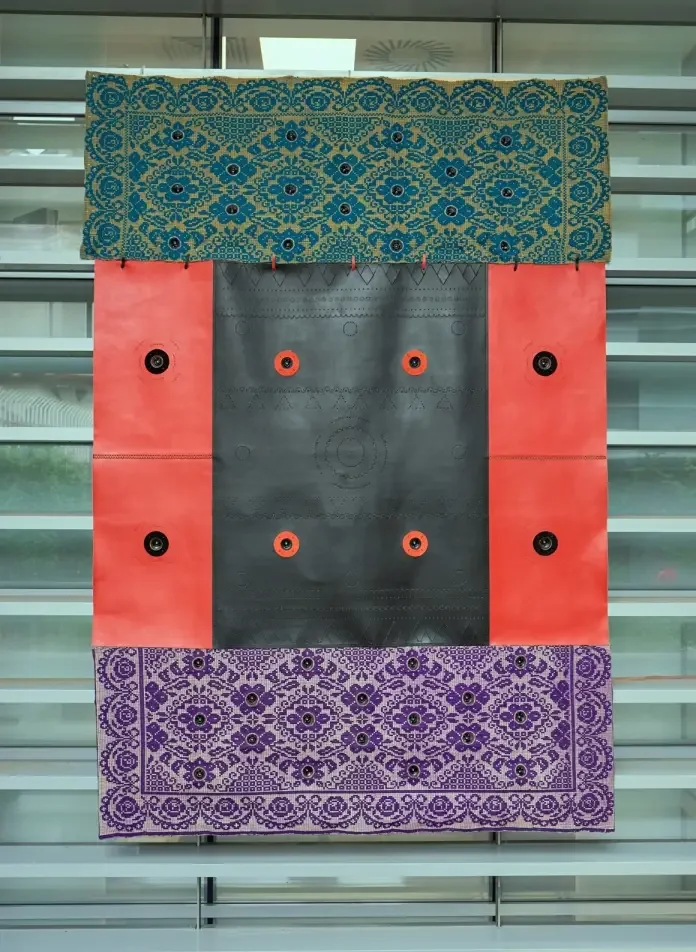 Un quadro decorativo composto da tessuti e bottoni, con sezioni di stoffa turchese, rossa e viola, e dettagli di bottoni neri e arancioni.