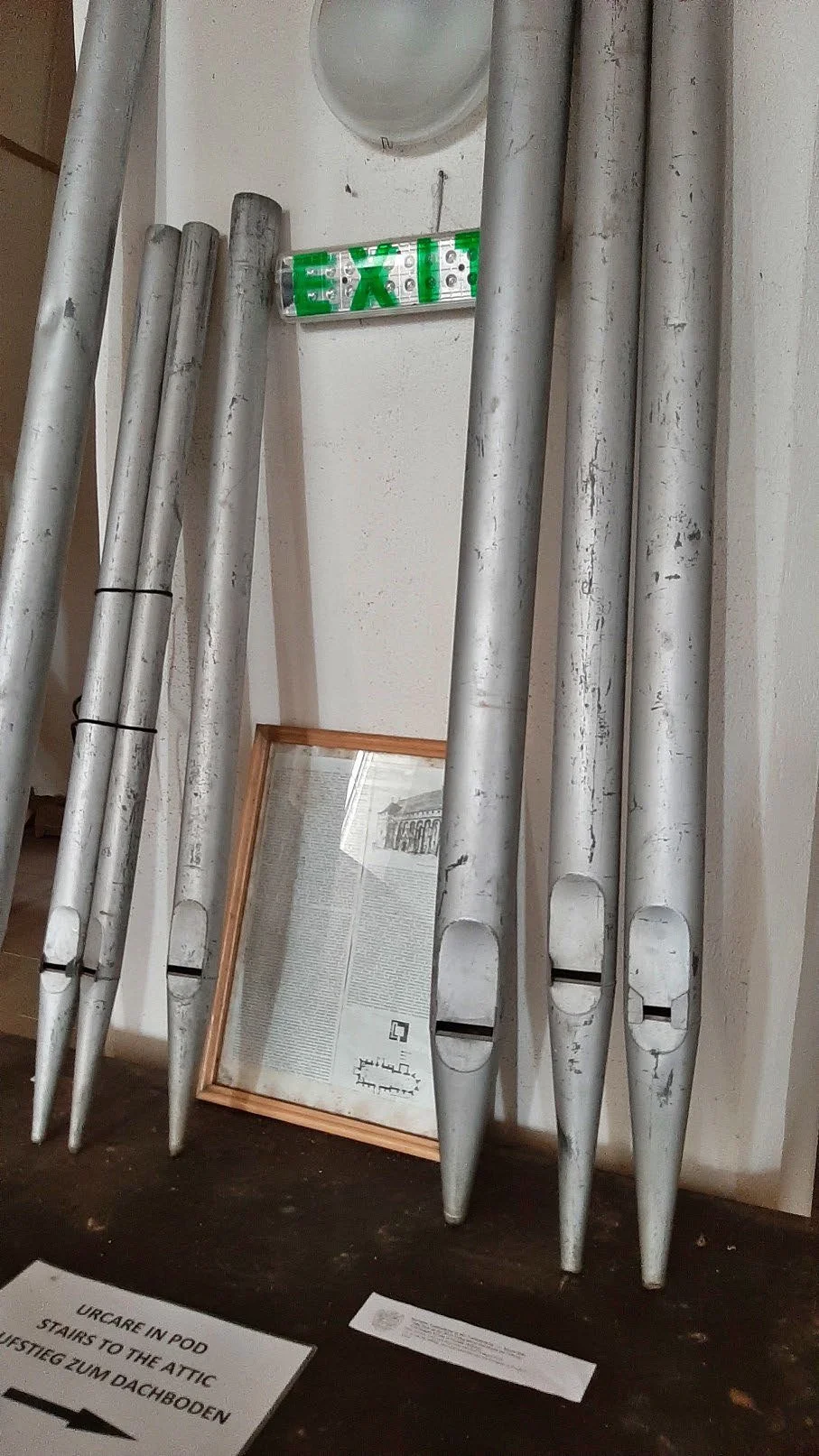 Bastoni di luci al neon e un quadro con testo in una stanza, con un segnale di uscita di emergenza sopra.