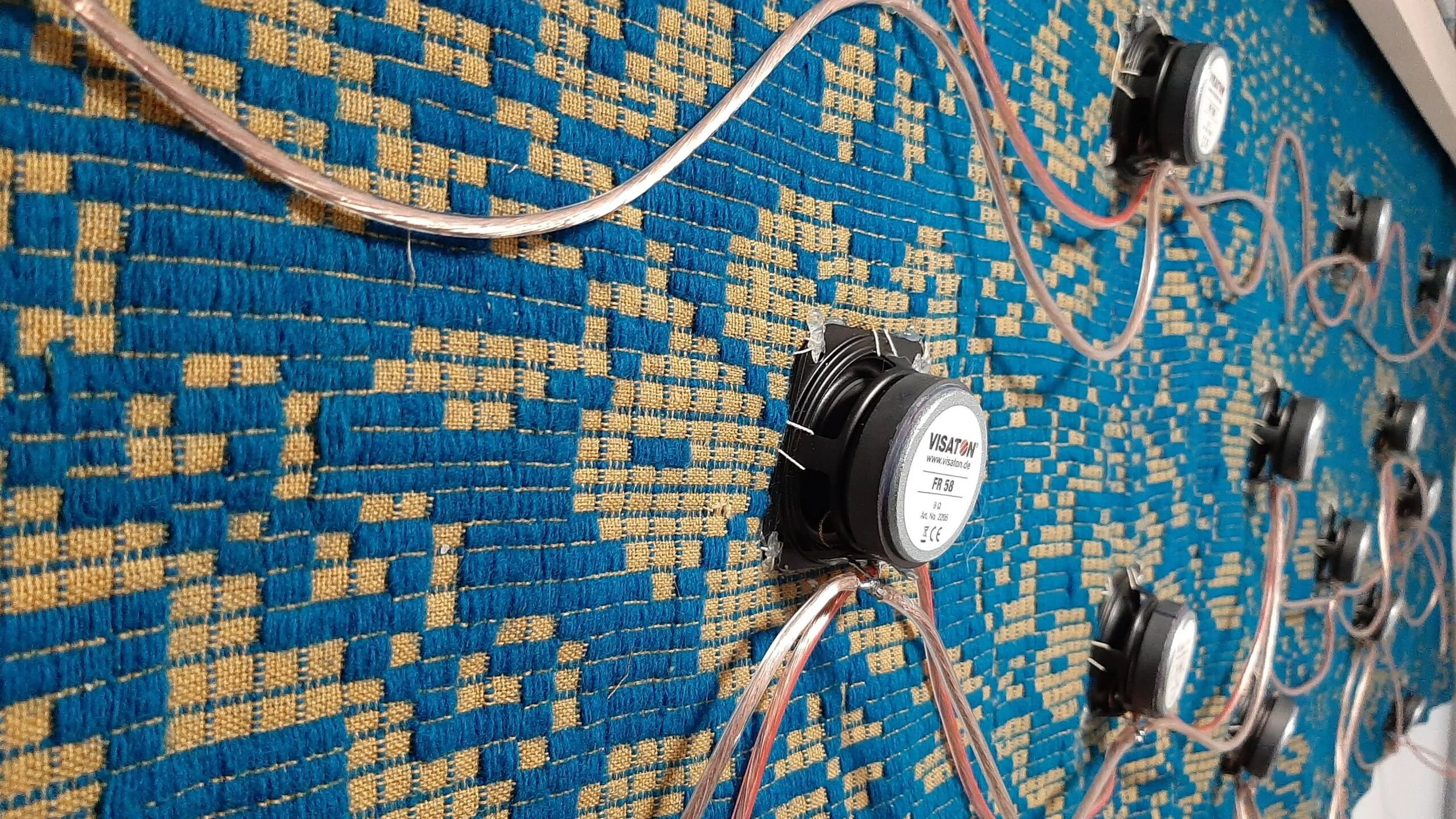 Foto di un circuito elettronico con diversi altoparlanti collegati a fili trasparenti su un tappeto blu e giallo.