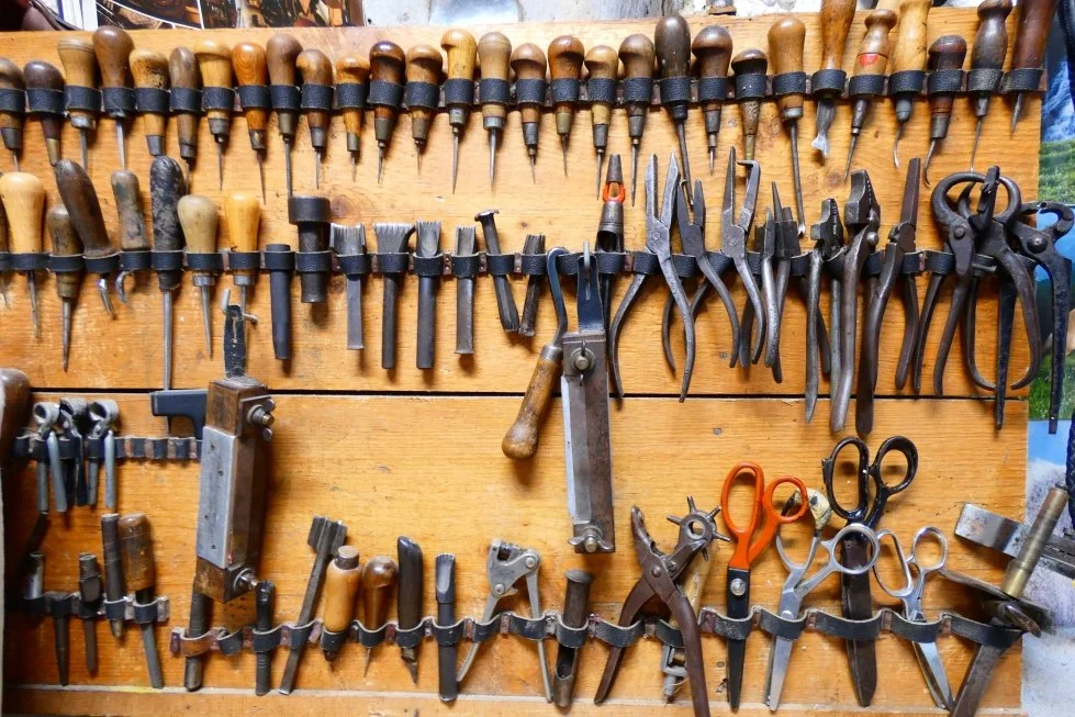 Attrezzi da ferramenta appesi a un supporto di legno, inclusi scalpelli, pinze, forbici e altri strumenti manuali.