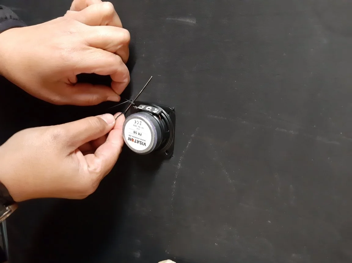 Una coppia di mani lavora su un sensore di una fotocamera, utilizzando un ago e filo per la riparazione, su una superficie di tavolo nera.