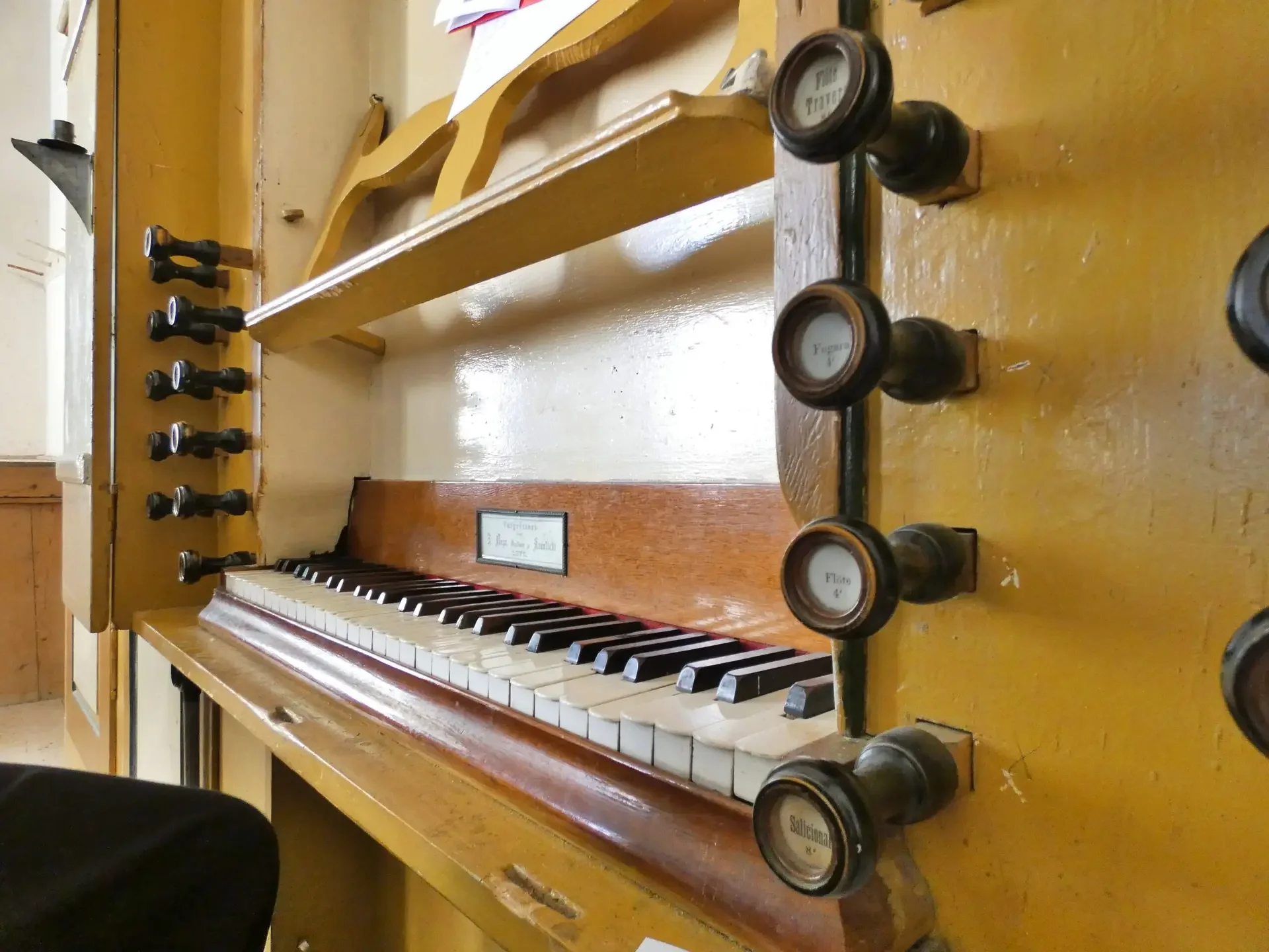 Piano vintage con tasti bianchi e neri, tasti di controllo, e manopole per regolazioni, in un ambiente di legno.