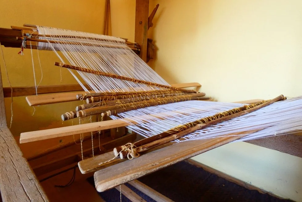 Un telaio per tessitura in legno con fili bianchi, situato in una stanza con pareti gialle.