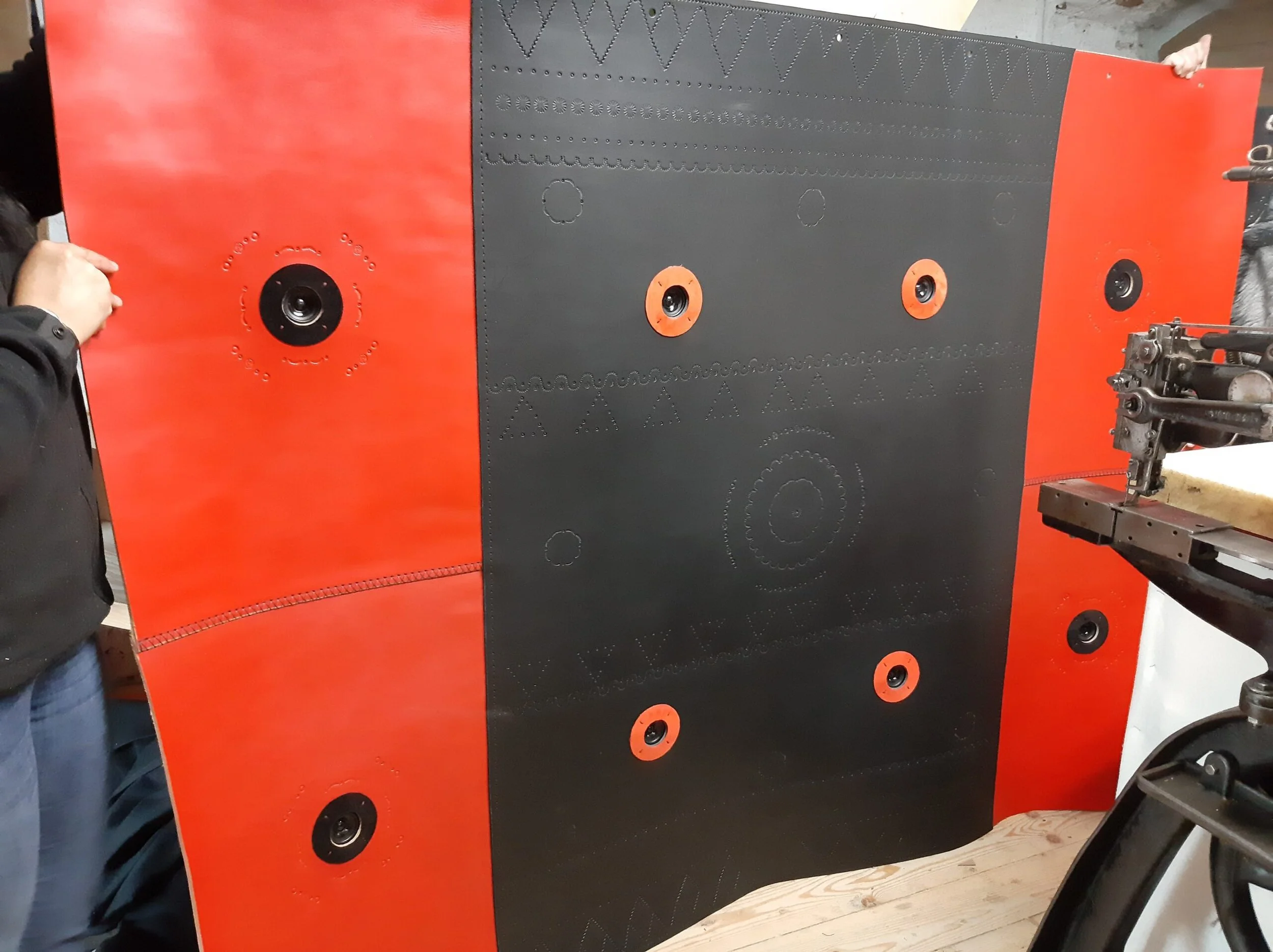 Un pannello di materiale nero e rosso con fori e tacche per fissaggi, e una persona che lavora con una macchina utensile.