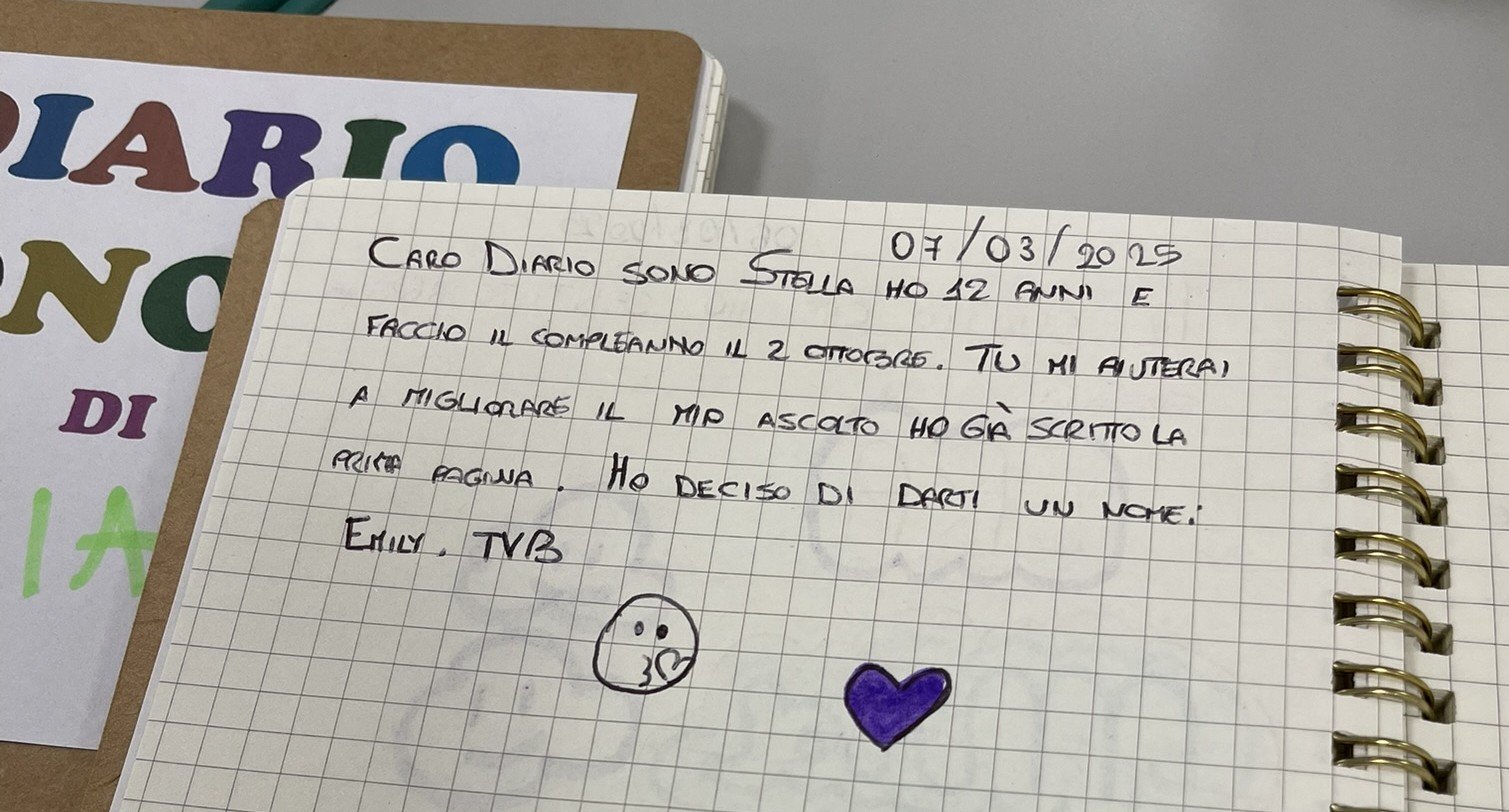 Un quaderno aperto con una nota scritta a mano, datata 07/03/2025, in italiano, con due disegni, uno di un volto con la lingua e uno di un cuore viola. Sullo sfondo si vede una parte di un altro quaderno colorato con lettere colorate.