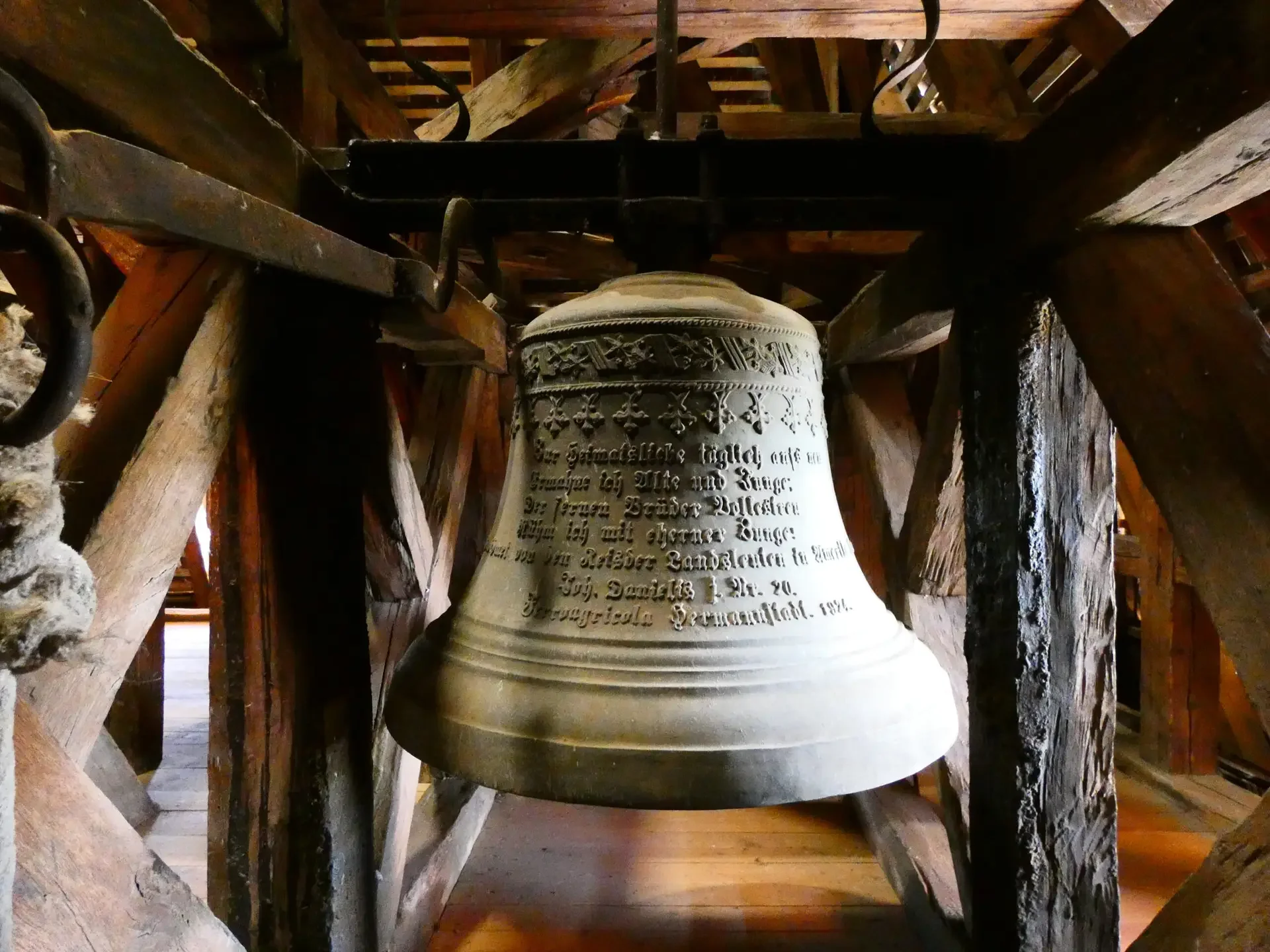 Campana di chiesa di metallo con incisioni in tedesco, inserita in un telaio di legno.