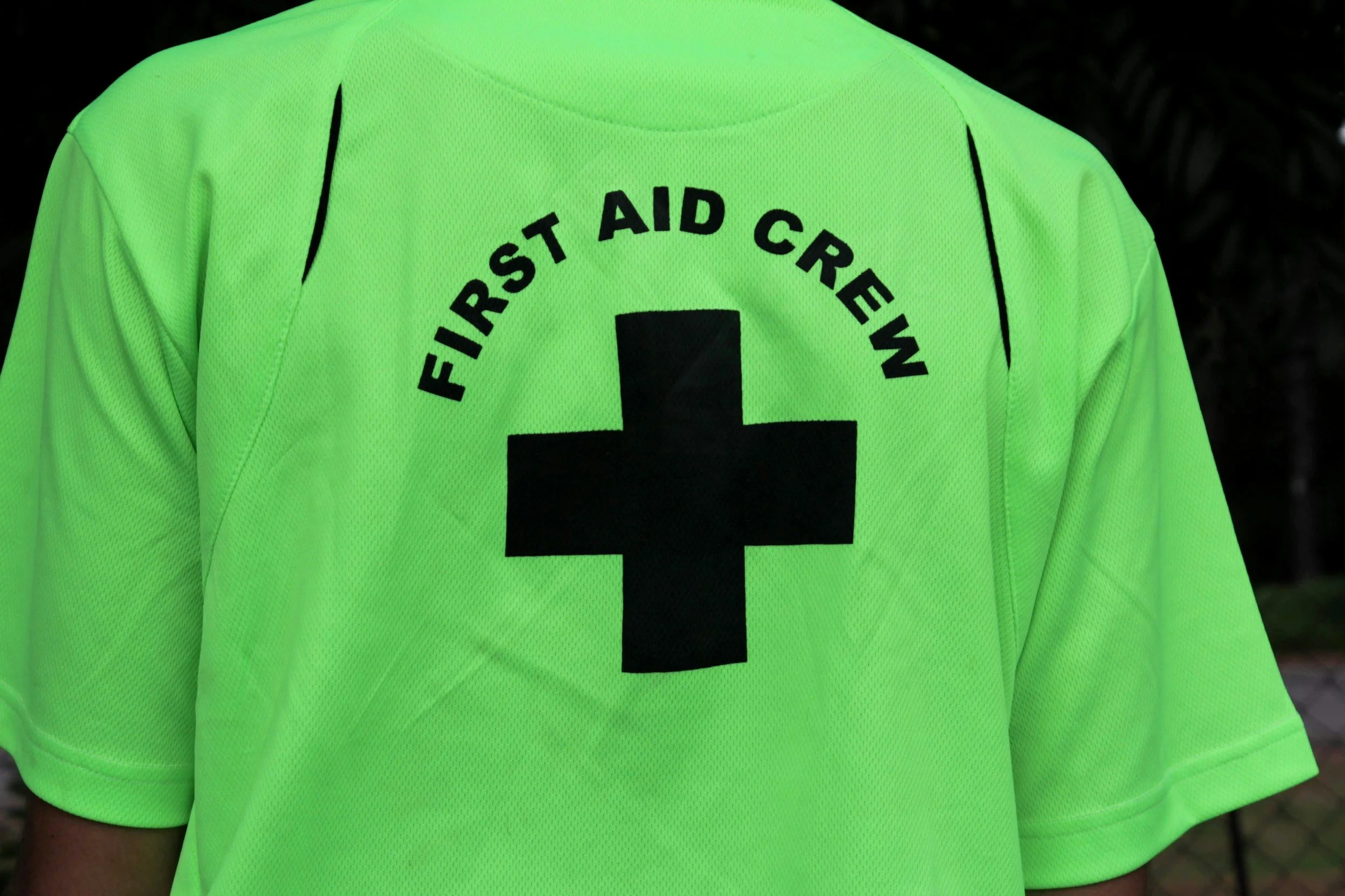 Close-up of a person wearing a fluorescent green First Aid Crew shirt with a black cross on the back.