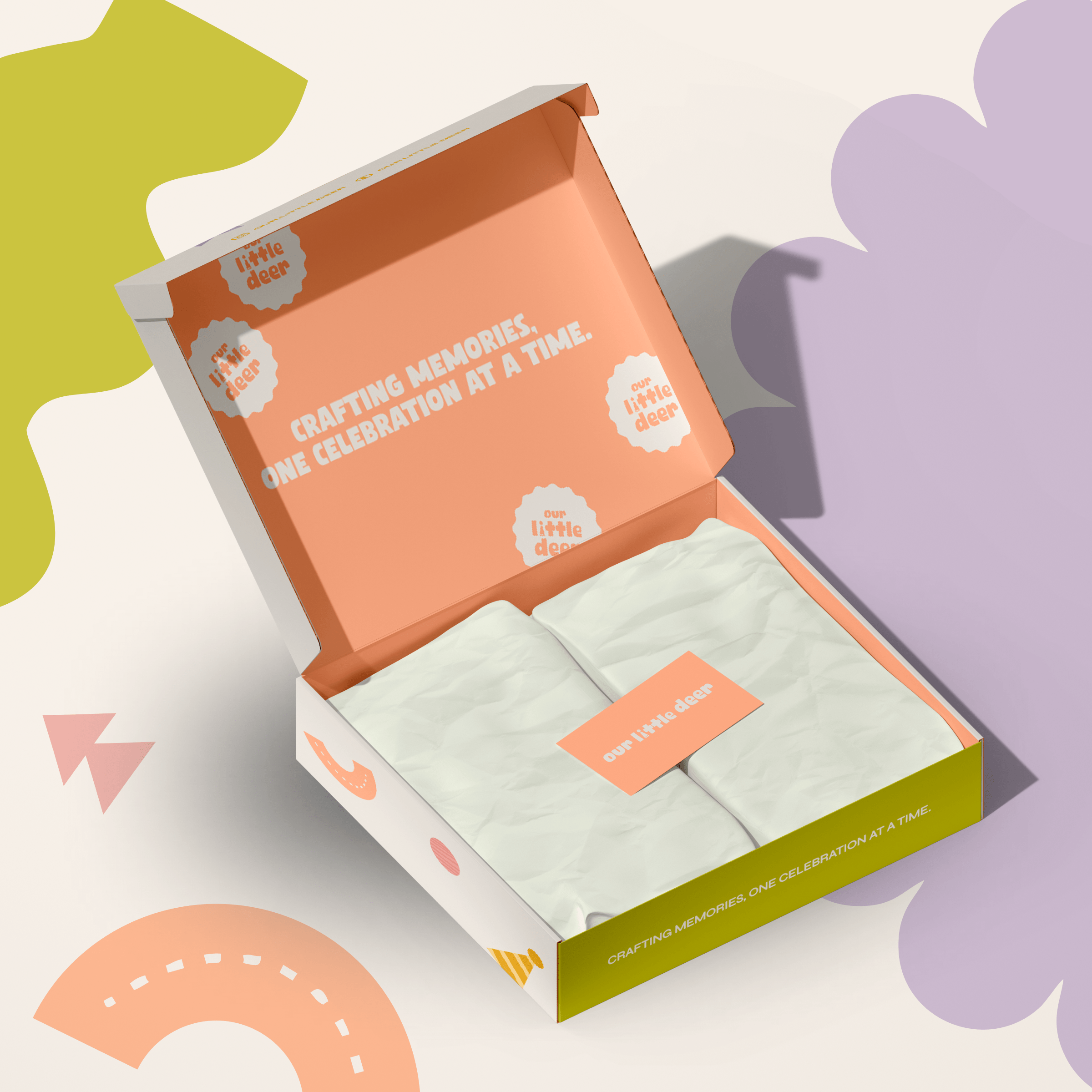Opened gift box with a peach and green design, containing two wrapped items, and the text "Crafting memories, one celebration at a time" on the inside lid. The box is branded with the phrase "our little deer."