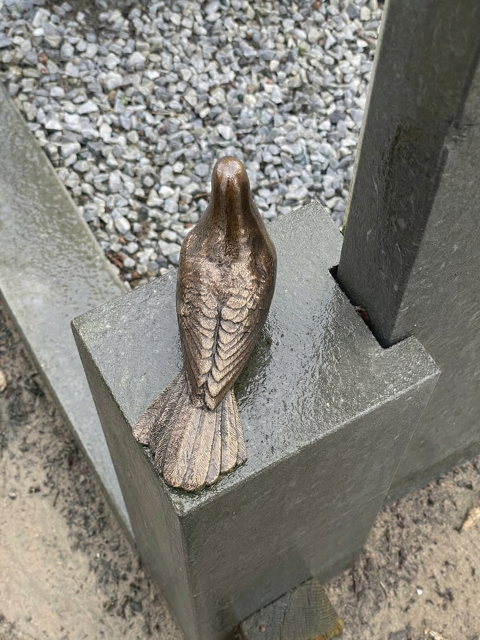 Bronskleurig vogelbeeld op een stenen pilaar, buiten.