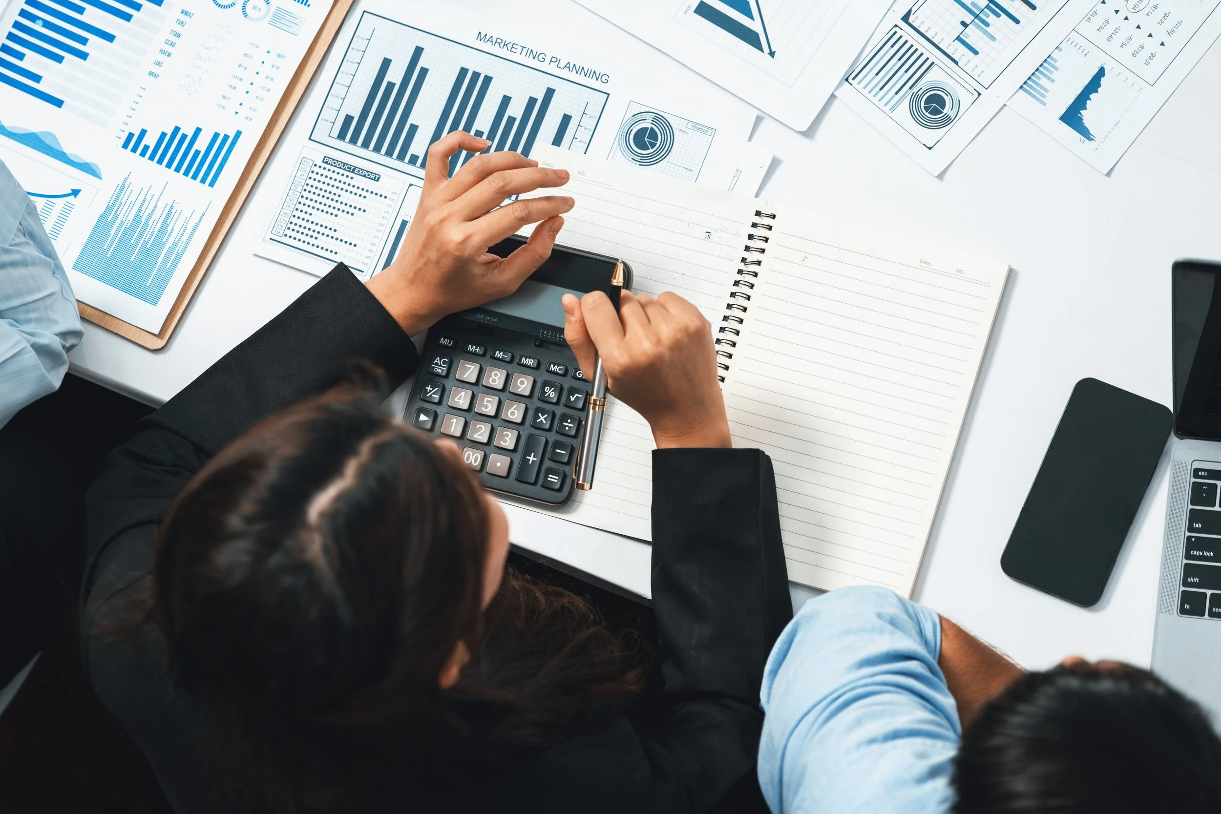 Photo of mountain range with reddish-brown peaks and snow patches, and a green grassy foreground, under a clear blue sky.
