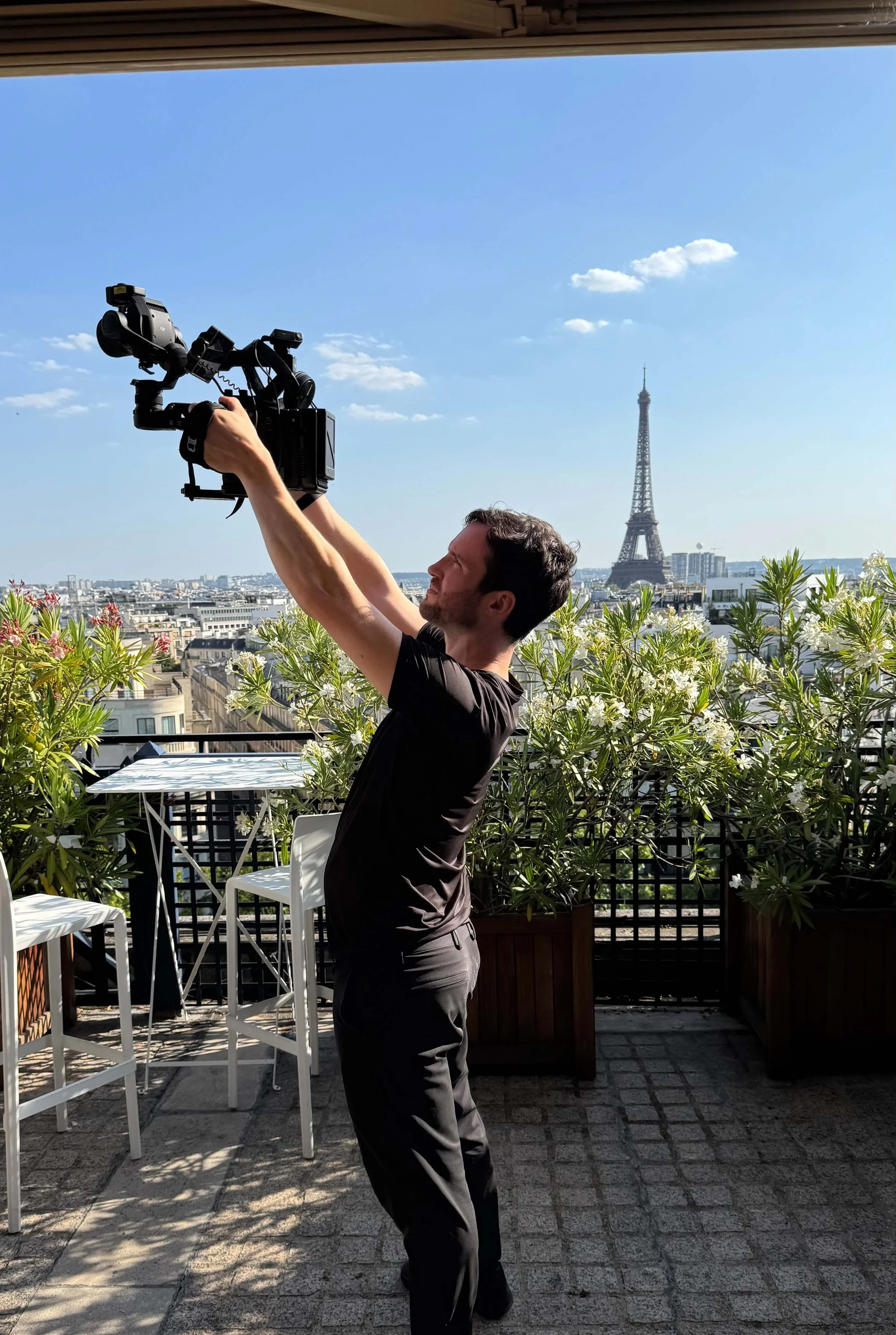 Robbie McKane is holding a professional video camera on a balcony in Paris. The Eiffel Tower is visible in the background.
