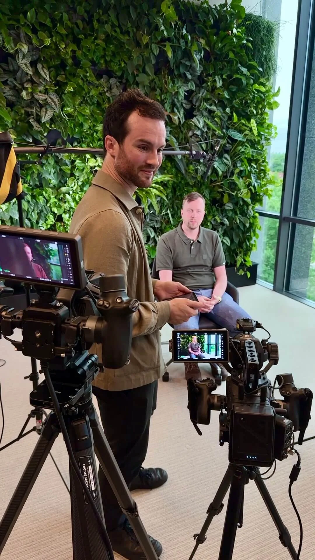 Robbie McKane stands to a 2 camera interview setup in an office smiling at an off-screen interviewer