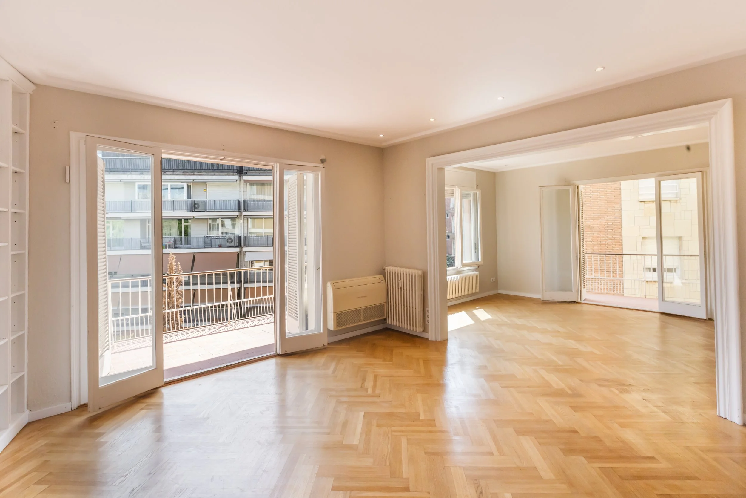 Sala de estar con paredes blancas, pisos de madera, chimenea y estantería de madera. Una pared con ventanas y un espejo grande de madera separado por marcos de madera.