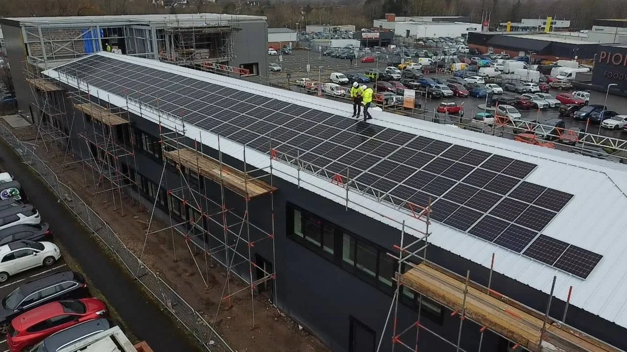 Construction workers installing solar panels on the roof of a building with scaffolding around it.