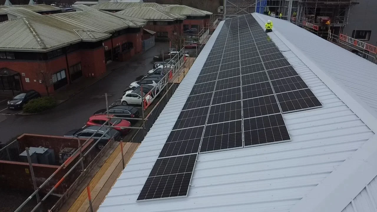 Workers installing solar panels on a white metal roof of a building
