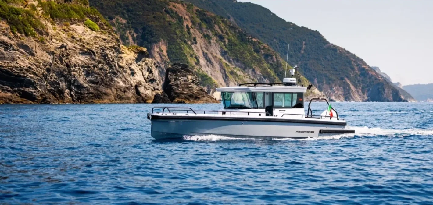 A motorboat sailing on calm water near a rocky, tree-covered shoreline.