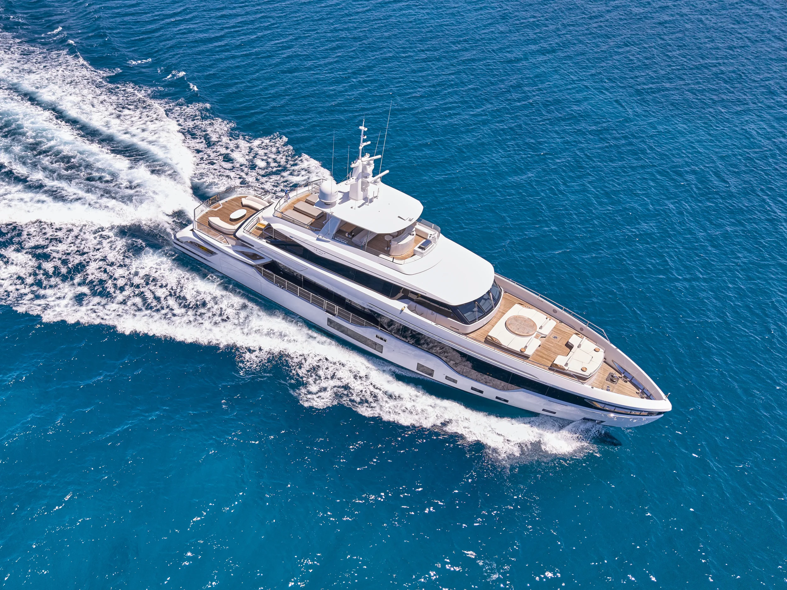 A large white yacht sailing on deep blue ocean water, creating a wake behind it.