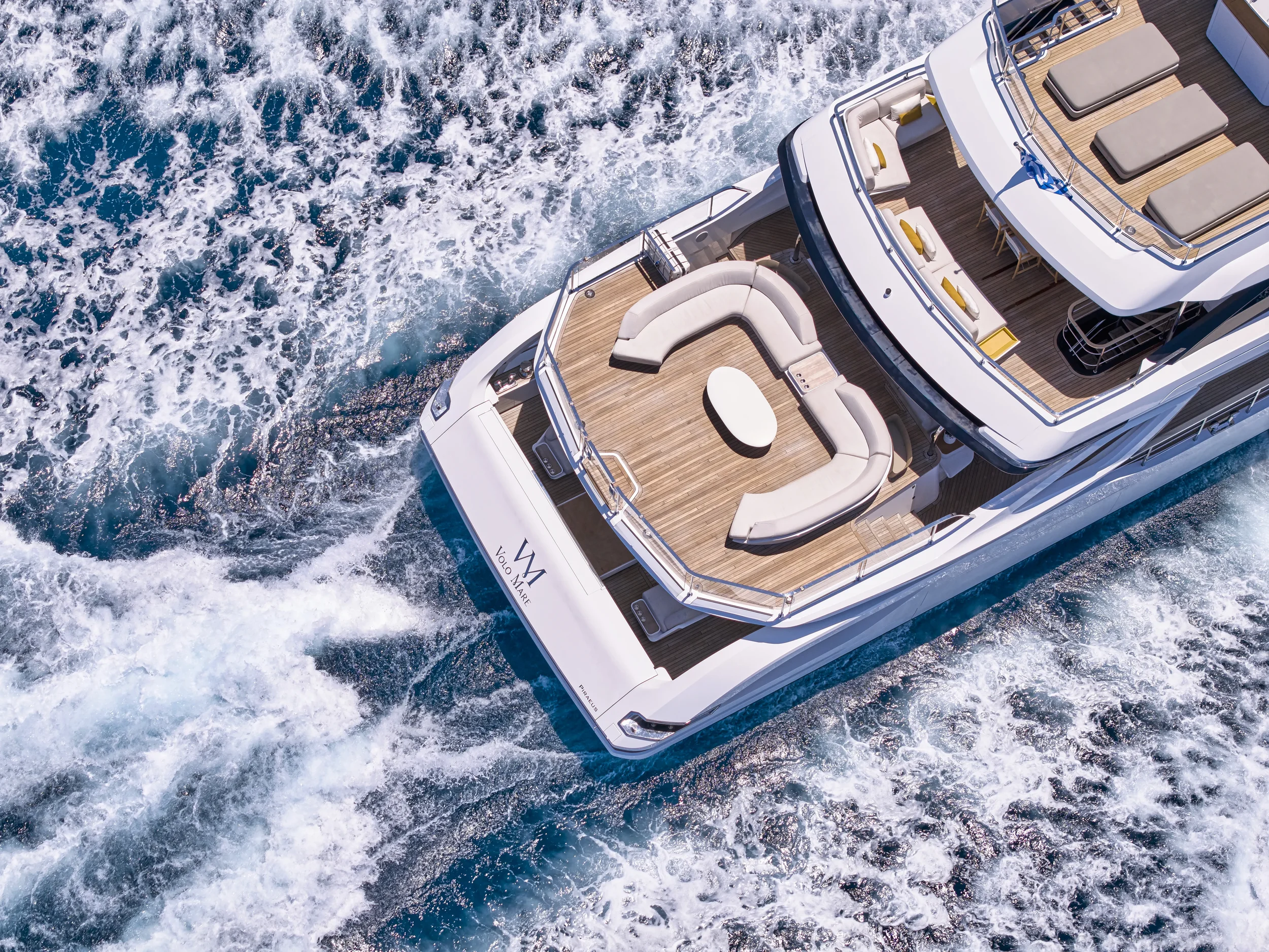Aerial view of a white luxury yacht sailing through blue ocean water with wake behind.