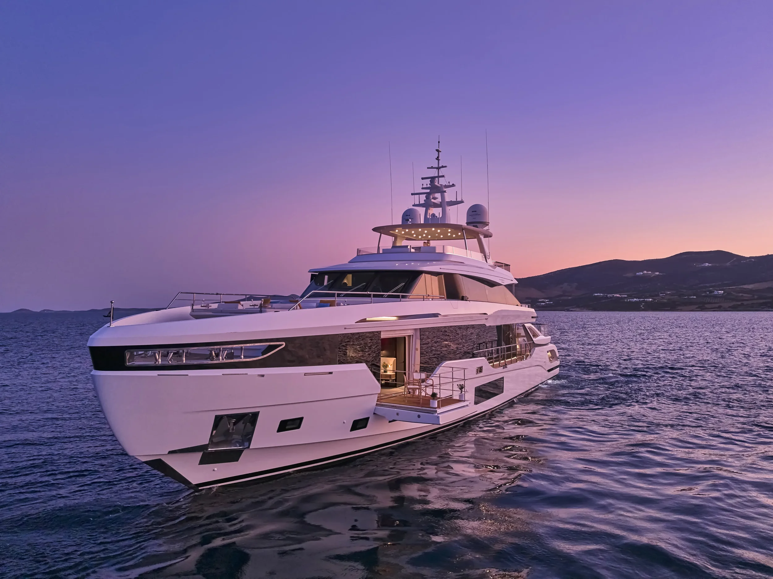 Luxury yacht sailing during sunset with hills in the background.
