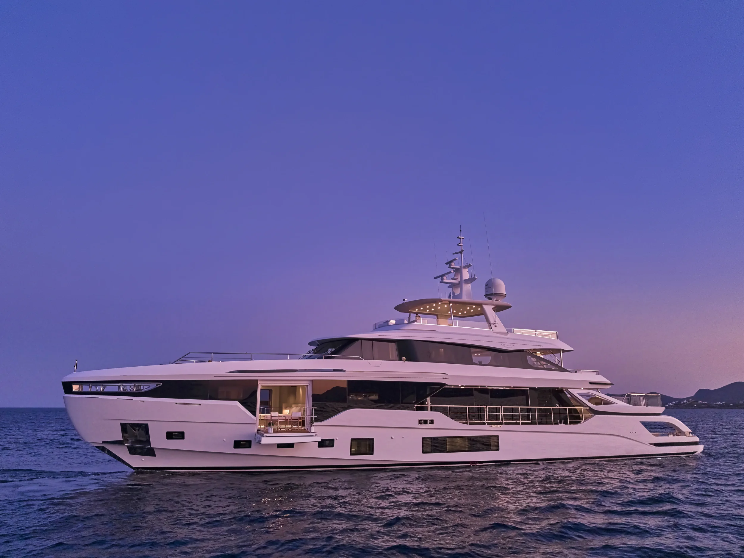 A large white yacht sailing on calm water during sunset or sunrise with a mountain in the background.