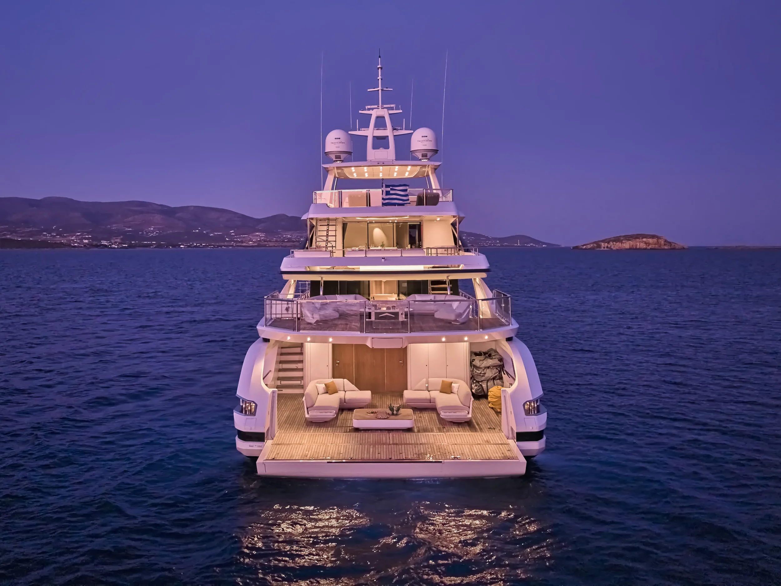 Luxury yacht anchored in calm water at dusk, with a mountainous landscape and islands in the background.