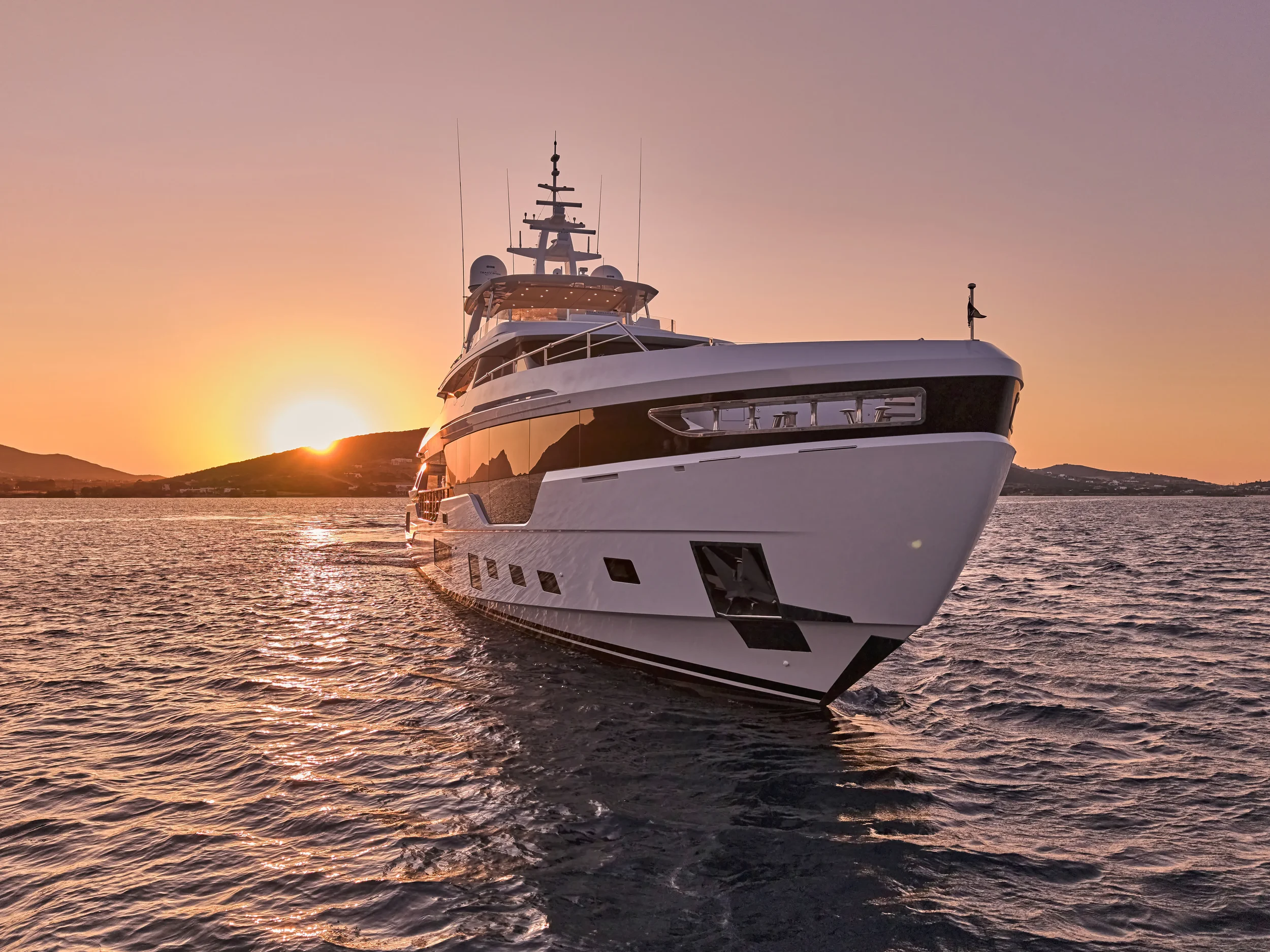 Luxury yacht sailing on calm ocean waters at sunset with hills in the background.