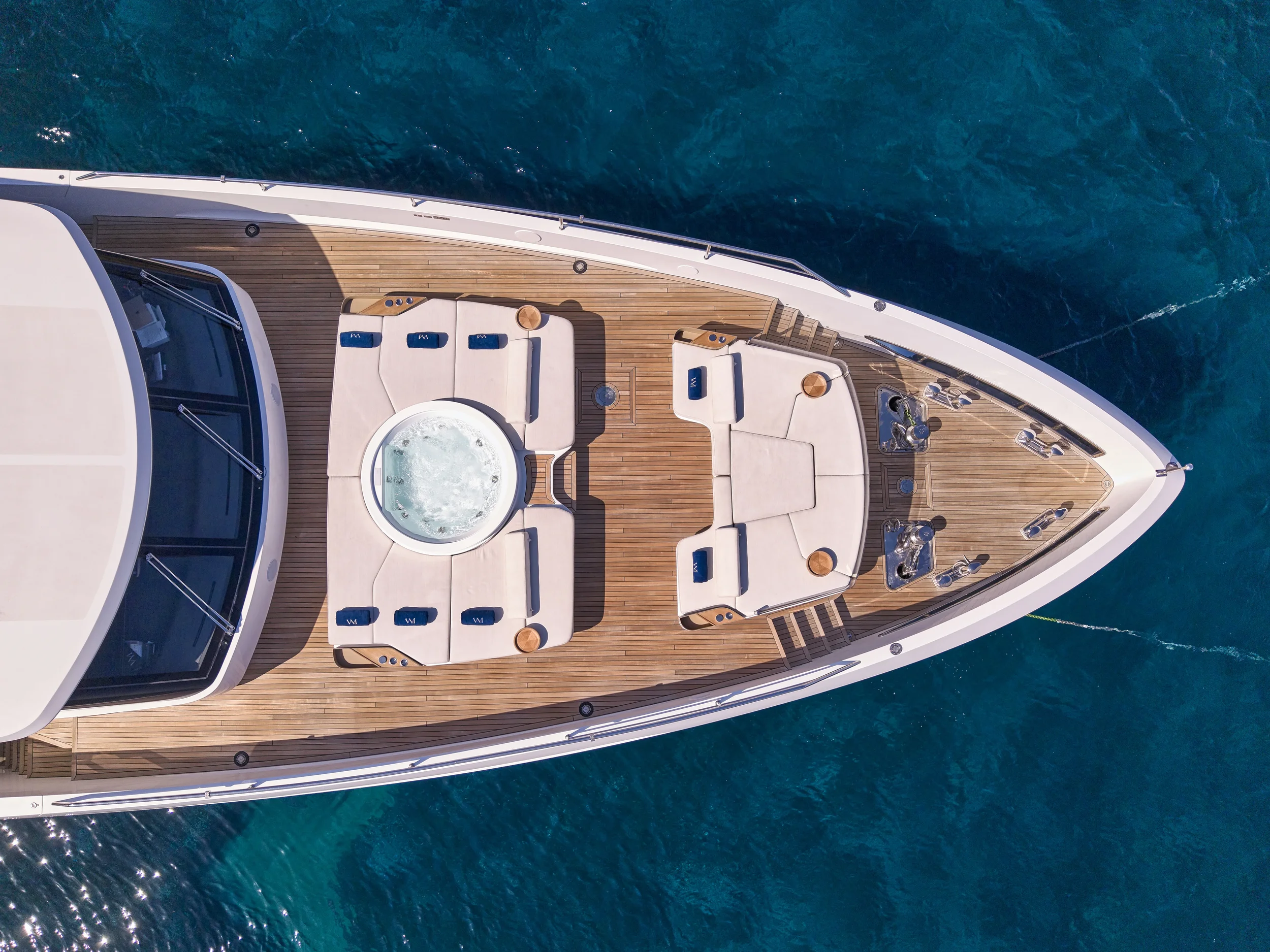 Top-down view of a luxury yacht's deck with a hot tub, seating area, and water in the background.