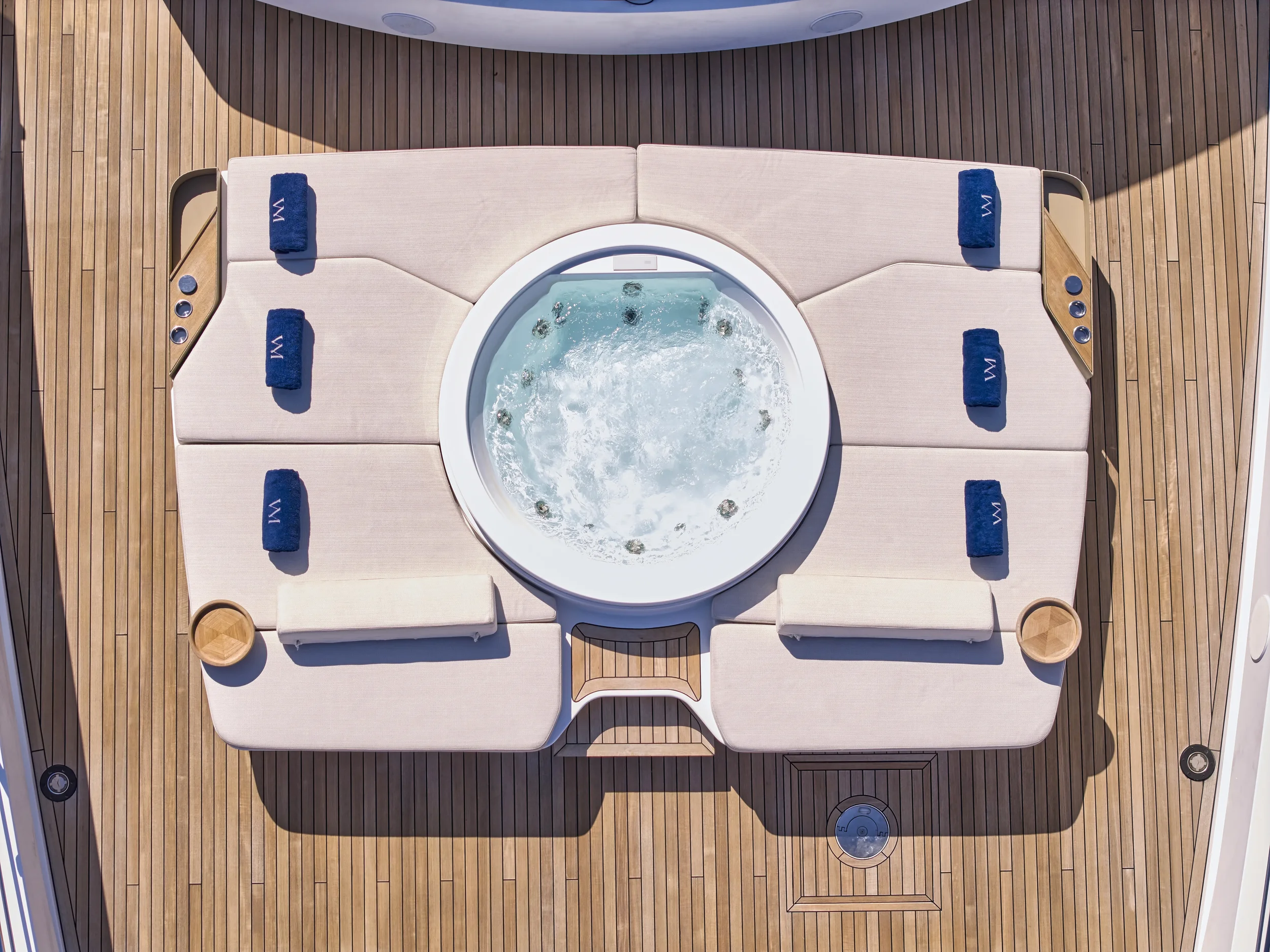 Top view of a hot tub on a boat deck surrounded by cushioned lounge chairs and blue towels.