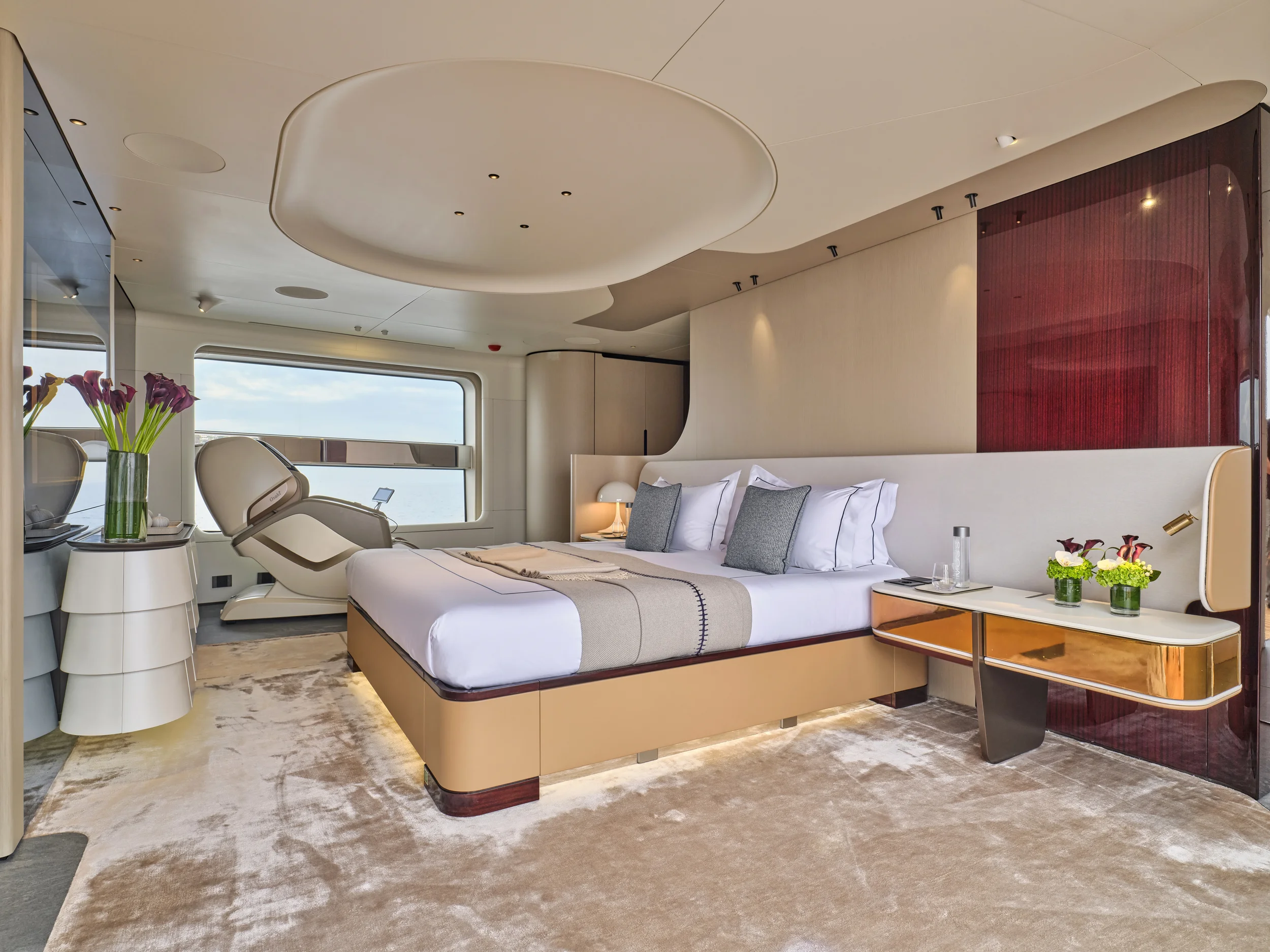 Luxury hotel room with a large bed, artwork, flowers, and a window offering ocean views.