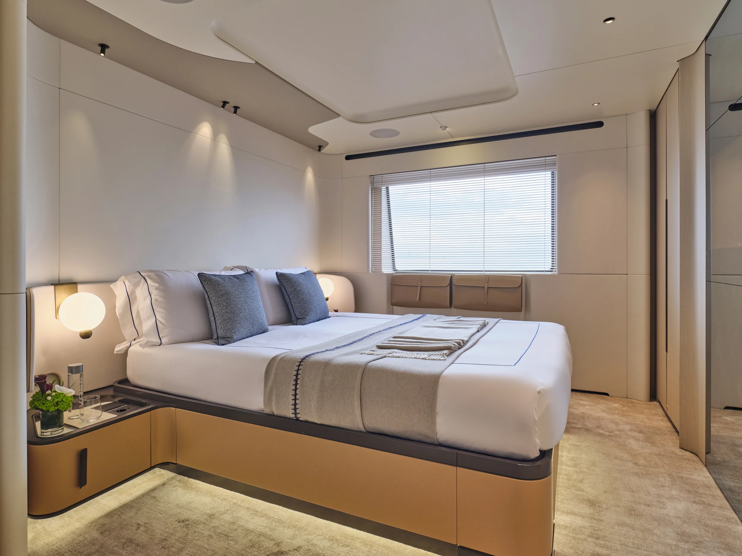 Modern bedroom with a large bed, white bedding, and two gray pillows, bedside lamps, a window with blinds, and minimal decor.