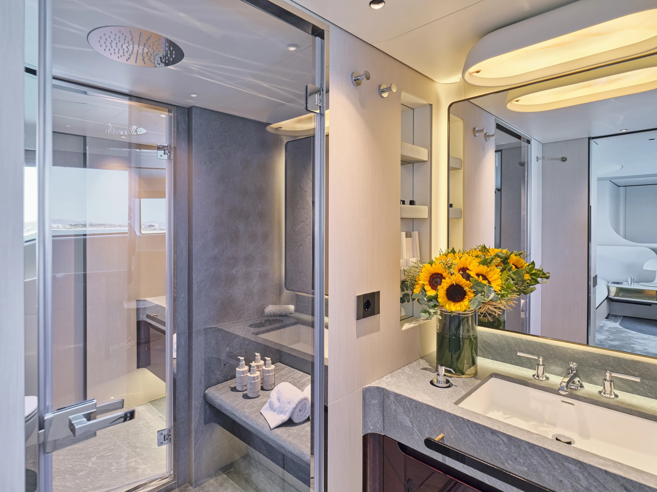 Modern bathroom with shower, sink, mirror, and a vase of sunflowers.