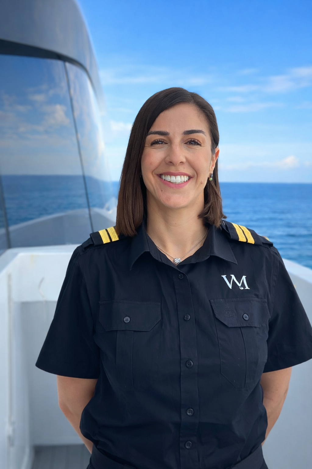 A woman in a navy uniform with shoulder epaulets and an embroidered letter 'W' on her shirt, standing outdoors near water and a modern bridge with a cityscape in the background.