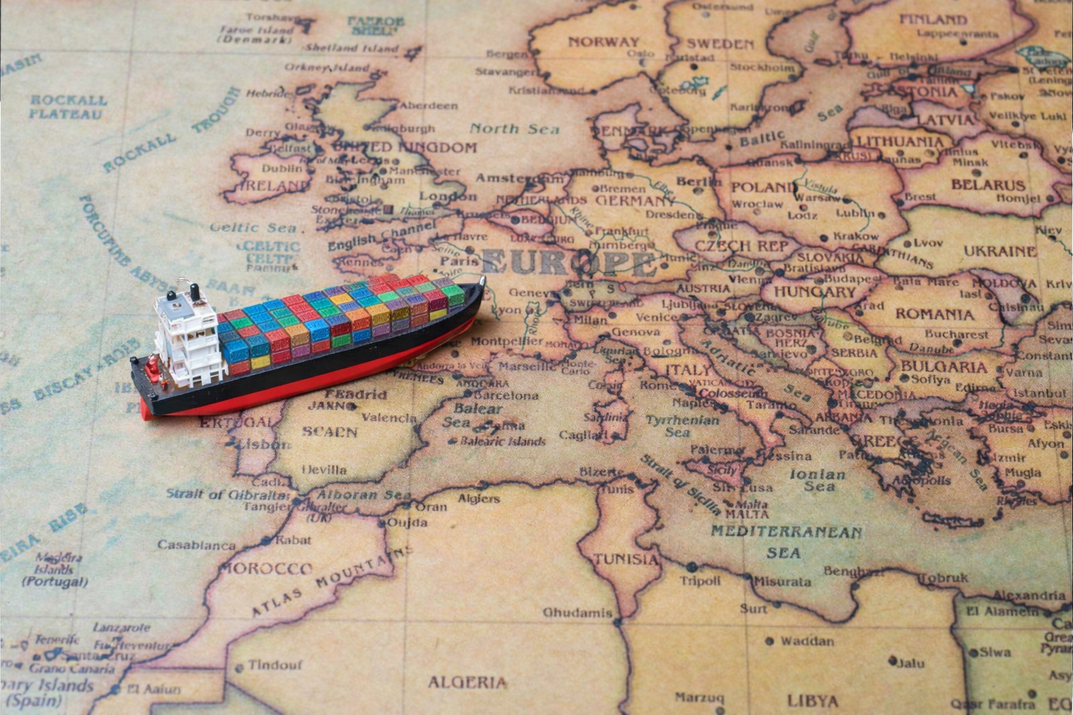 Miniature cargo ship with colorful containers placed on a vintage map of Europe and parts of Africa, Middle East, and Atlantic Ocean.