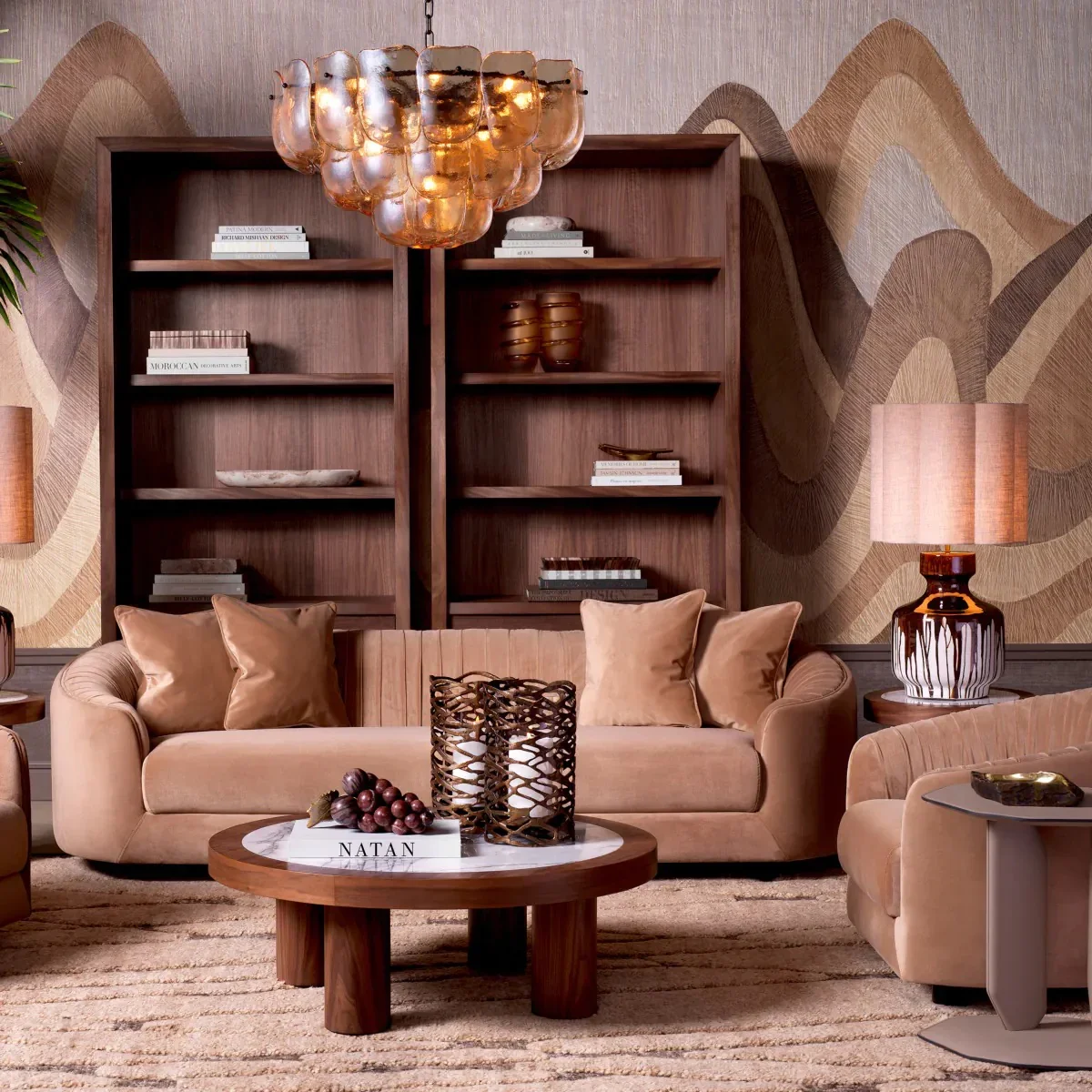 Living room with beige sofa and armchair, wooden coffee table with decorative candle holders and a bunch of grapes, large wall shelves with books and decorative items, a lamp, and a modern, textured wallpaper backdrop.
