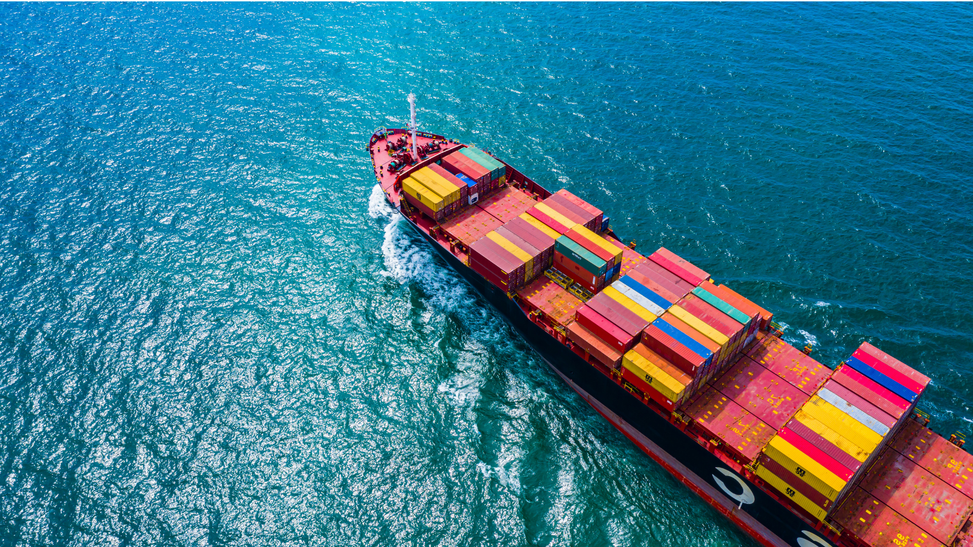 Aerial view of a cargo ship with colorful containers sailing in blue ocean water.