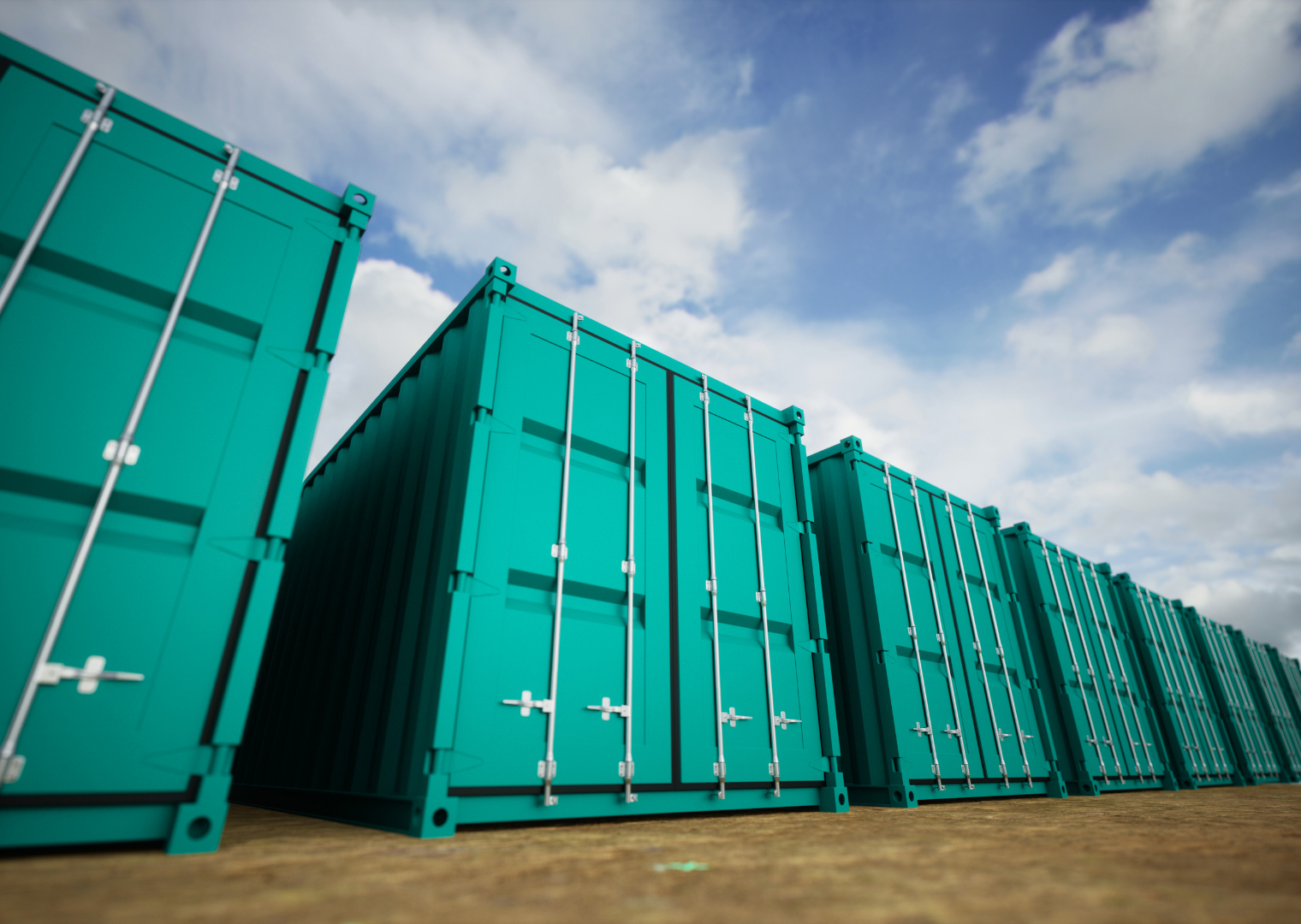 A row of teal shipping containers stacked outdoors under a partly cloudy sky.