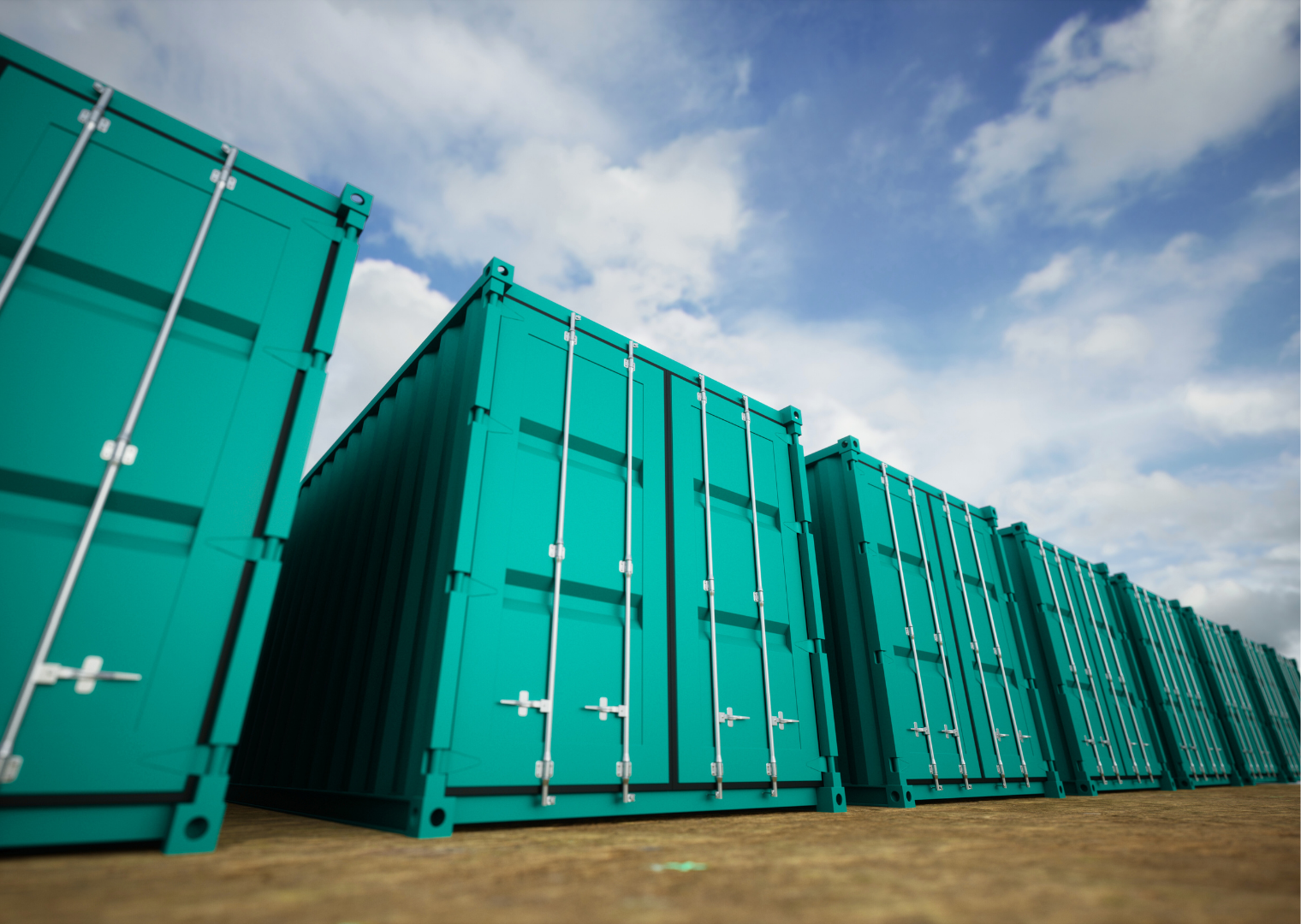Multiple teal shipping containers lined up outdoors against a partly cloudy sky.