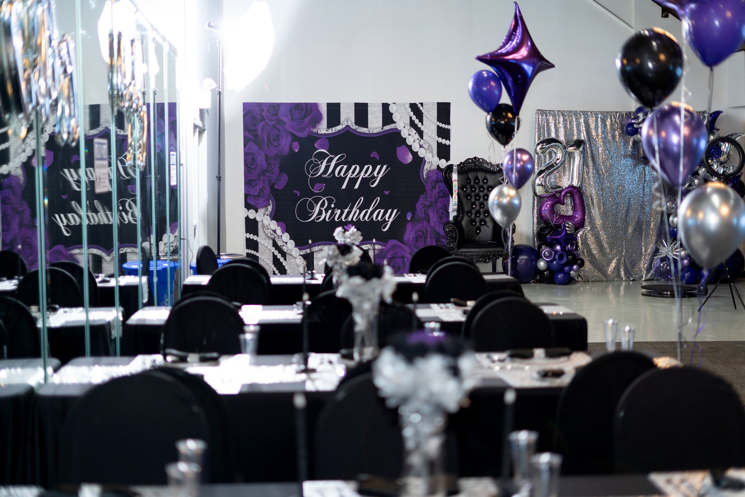 Decorated party room with balloons, purple roses, a 'Happy Birthday' sign, and a table set for celebration.