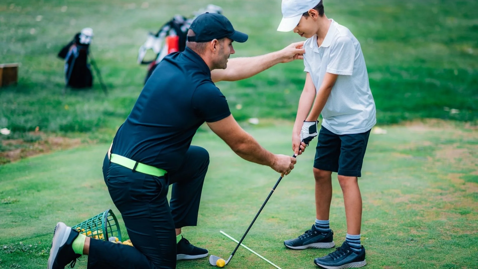A man helping a boy on a golf course with putting practice.