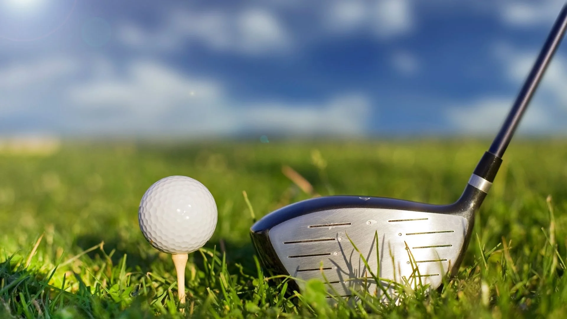 Close-up view of a golf club and golf ball on a tee, set on a grassy golf course under a cloudy sky.