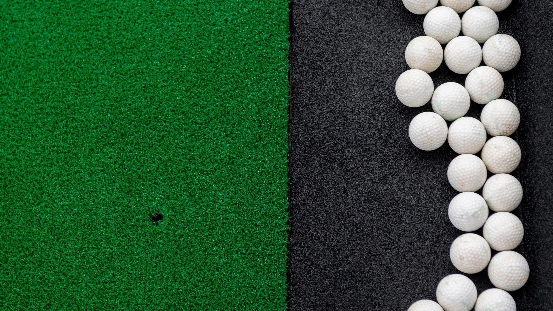Golf ball placement area on artificial grass, with dozens of white golf balls lined up on a black surface.