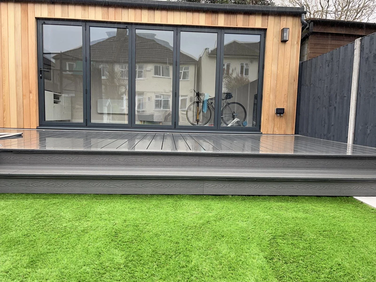 Modern backyard with a sliding glass door, wooden exterior, and artificial grass.