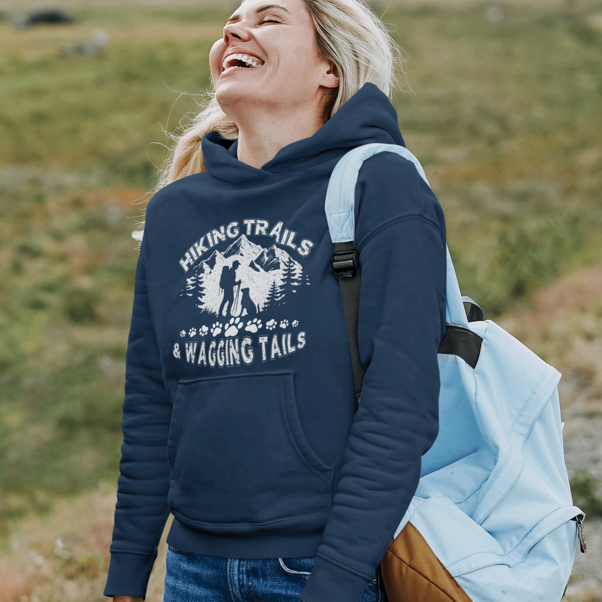 Woman smiling outdoors with a backpack, wearing a navy hoodie with hiking graphics.
