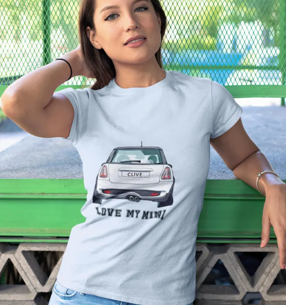 Woman wearing a light blue T-shirt with a car illustration and the text 'LOVE MY MINI' standing in front of a green park bench.