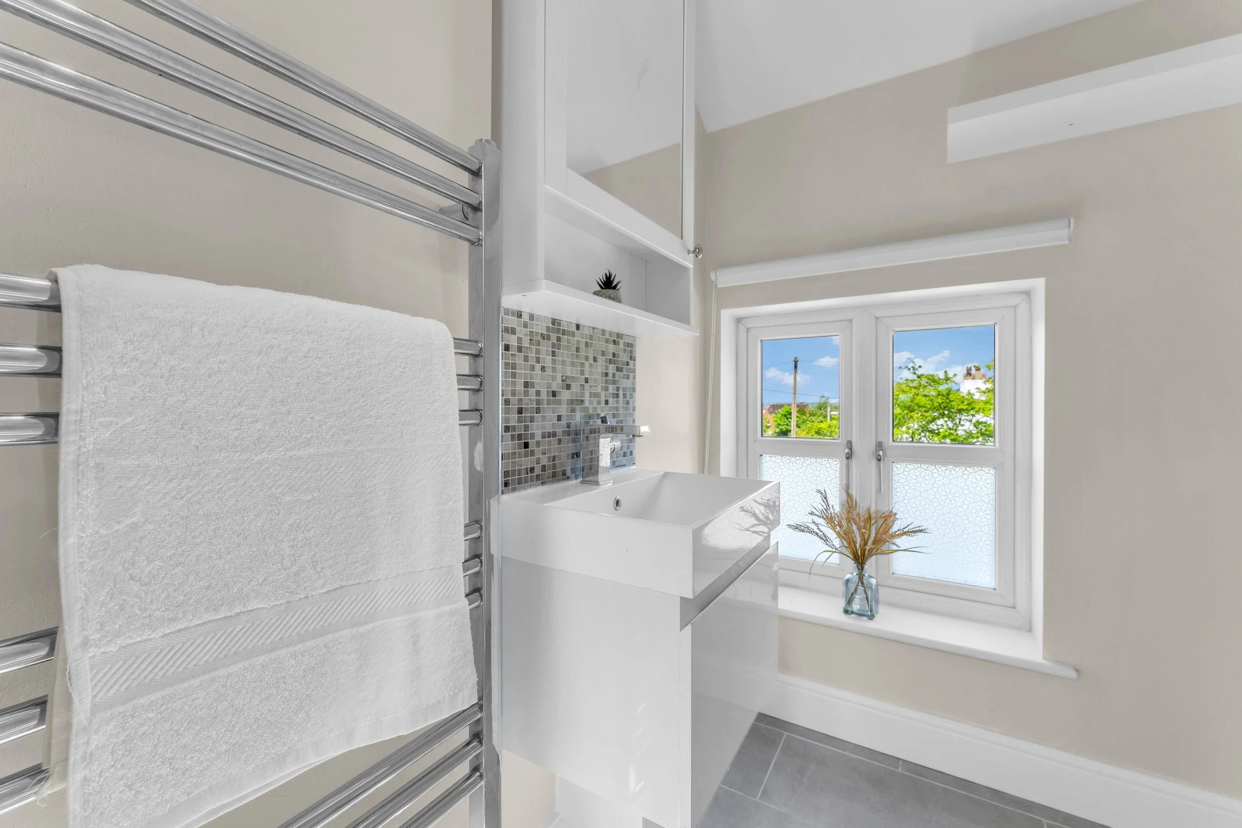Bright bathroom with a large window showing a sunny outdoor scene, white sink, and a towel rack with a white towel.