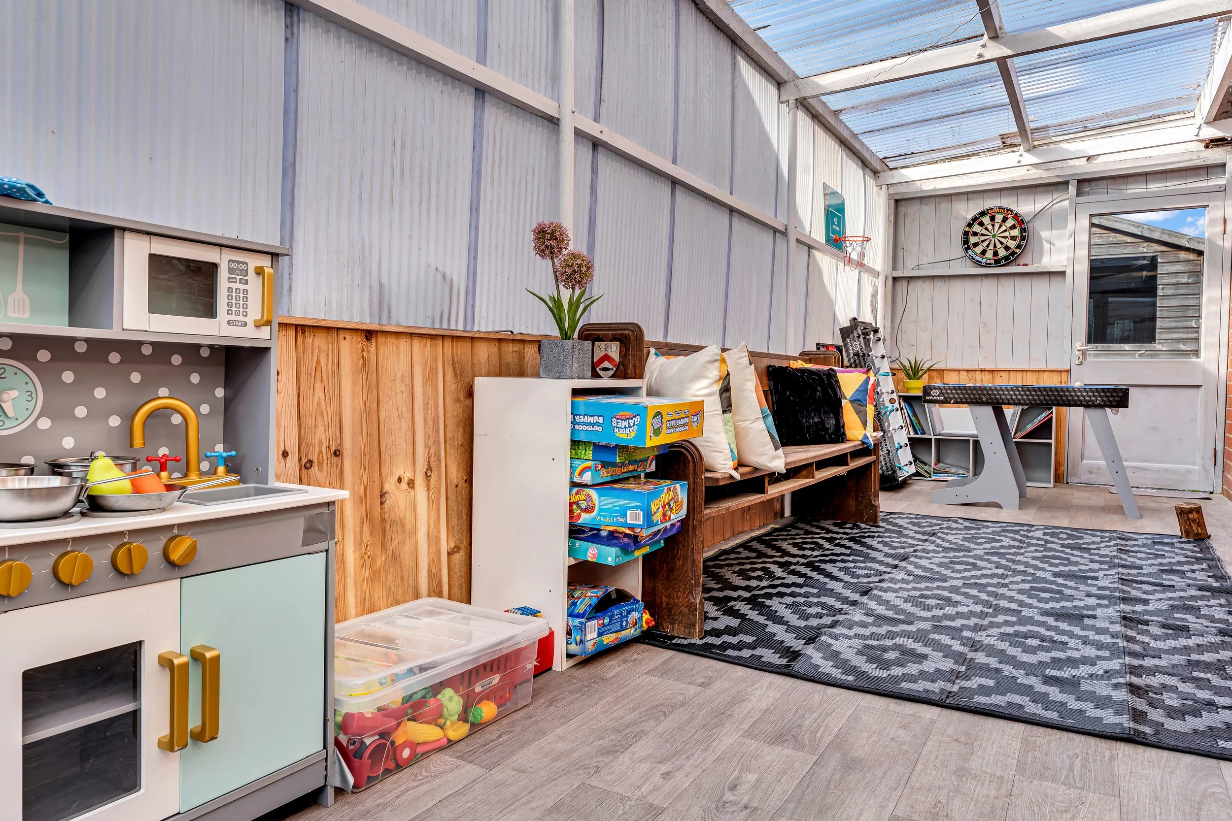 Indoor play area with toy kitchen, board games, pillows, plant, dartboard, books, and a foosball table.