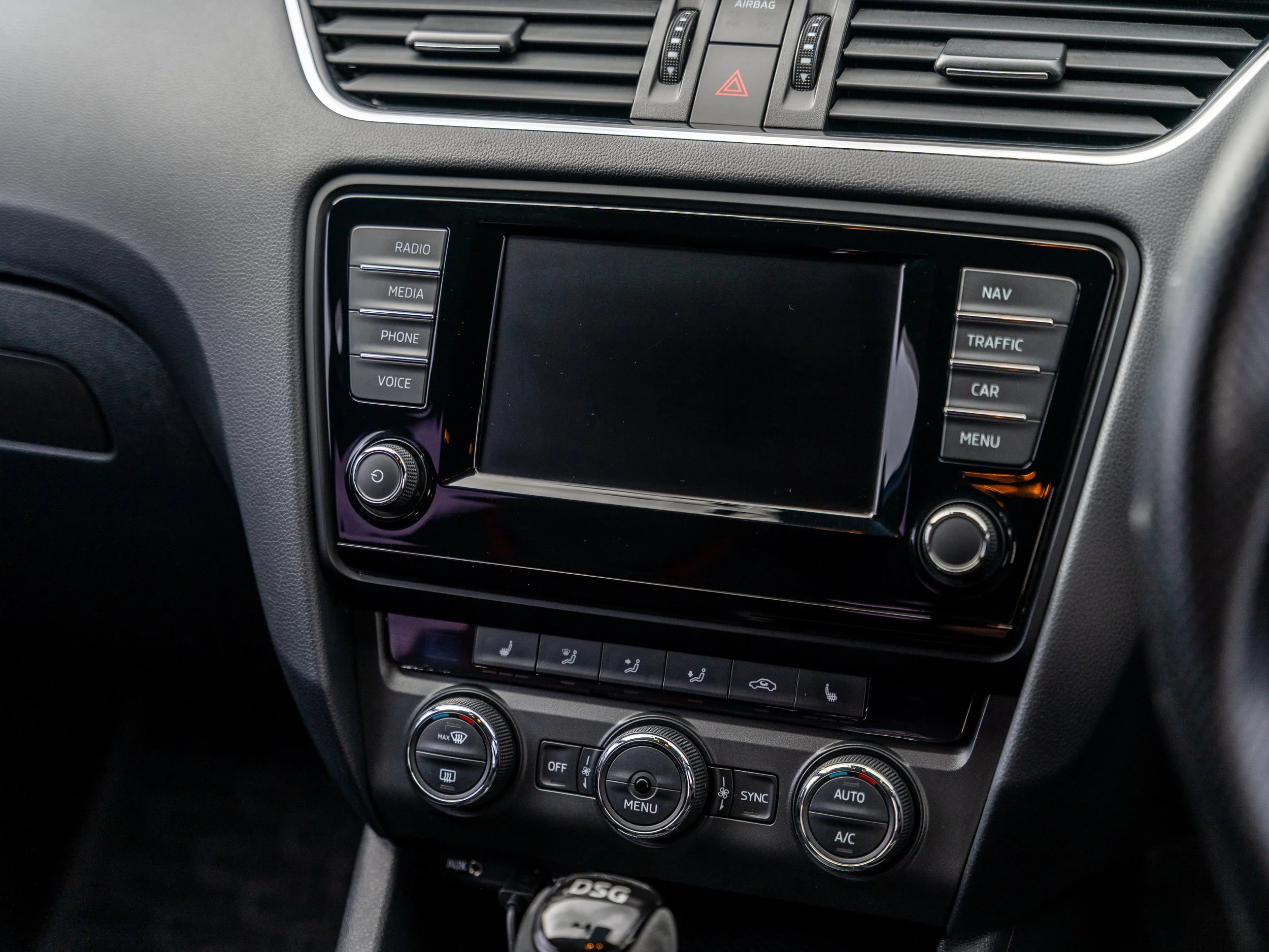 Car dashboard touchscreen display with various control buttons and climate controls below, in a vehicle interior.