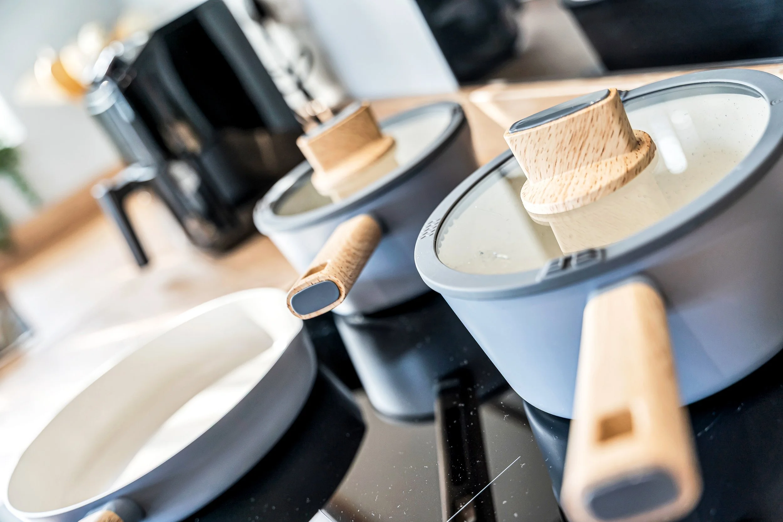 Three Nordic cookware pots with glass lids and wooden handles on a black countertop in a kitchen.