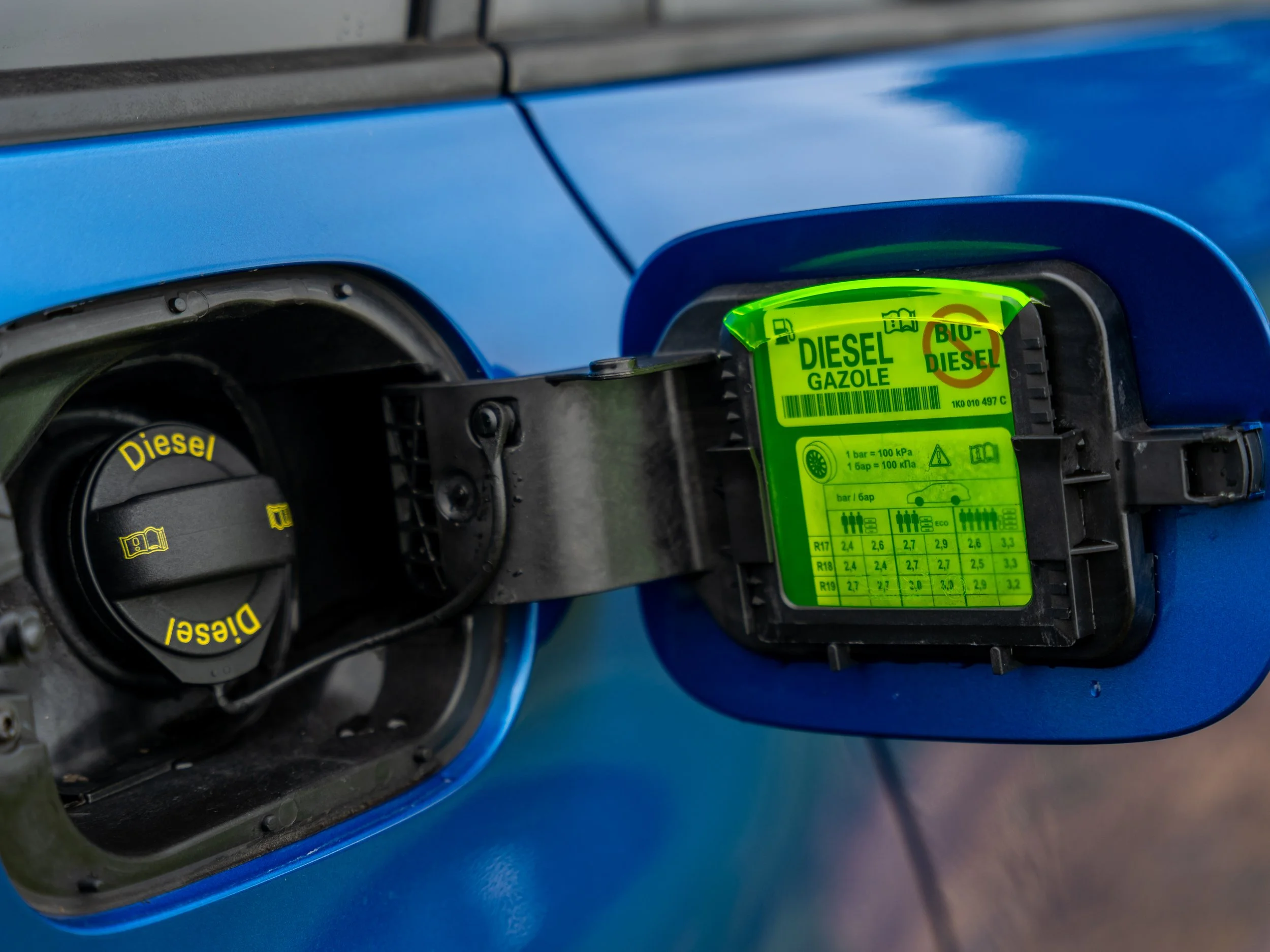 The fuel cap of a blue vehicle with a green label indicating bio-diesel fuel, next to a black diesel cap labeled 'Diesel'.