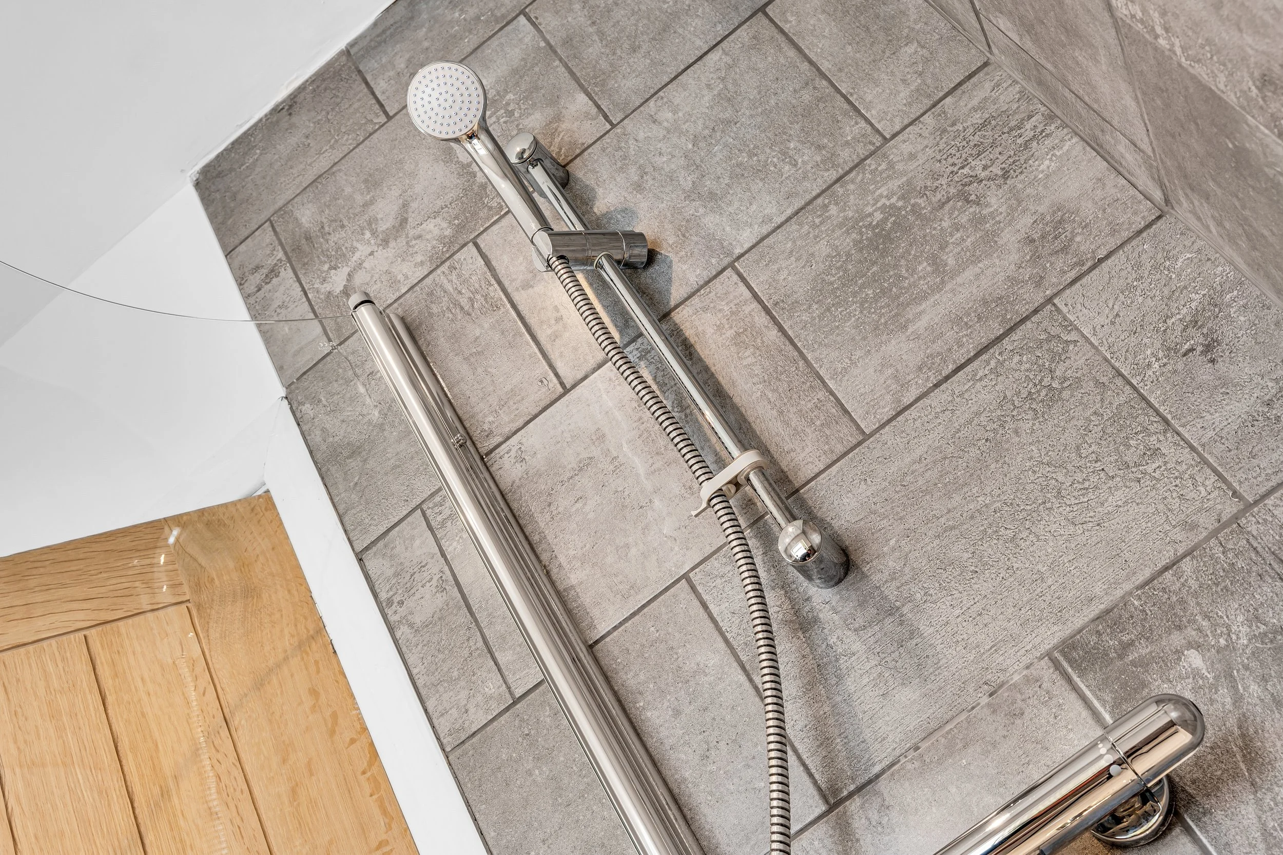 Metal shower head and rails with flexible hose mounted on tiled wall in bathroom.